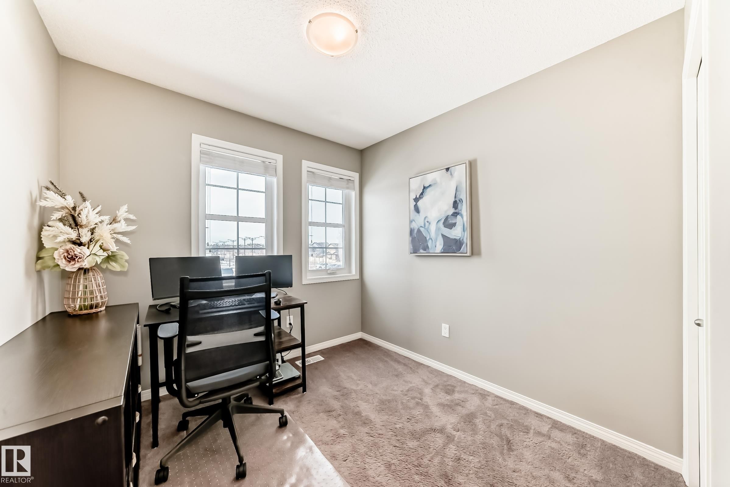 This room features a neutral color palette, two windows providing natural light, and carpeted flooring - 86 4029 Orchards Drive, Edmonton, AB - Indoor Photo Showing Office