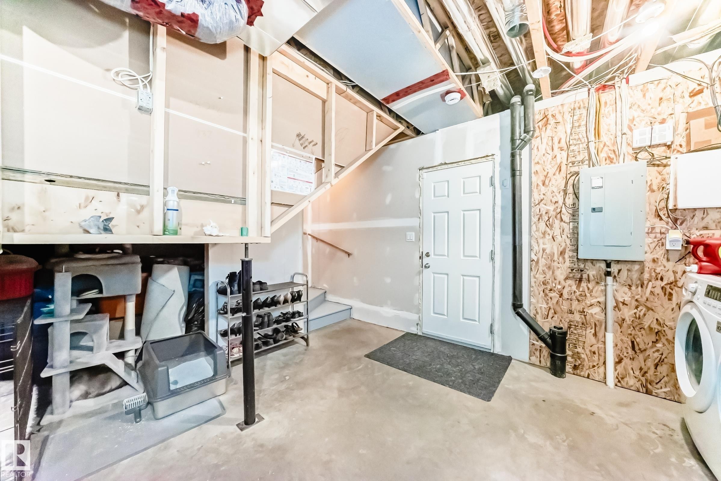 Unfinished space with a concrete floor, exposed ceiling joists, and a white paneled door - 86 4029 Orchards Drive, Edmonton, AB - Indoor