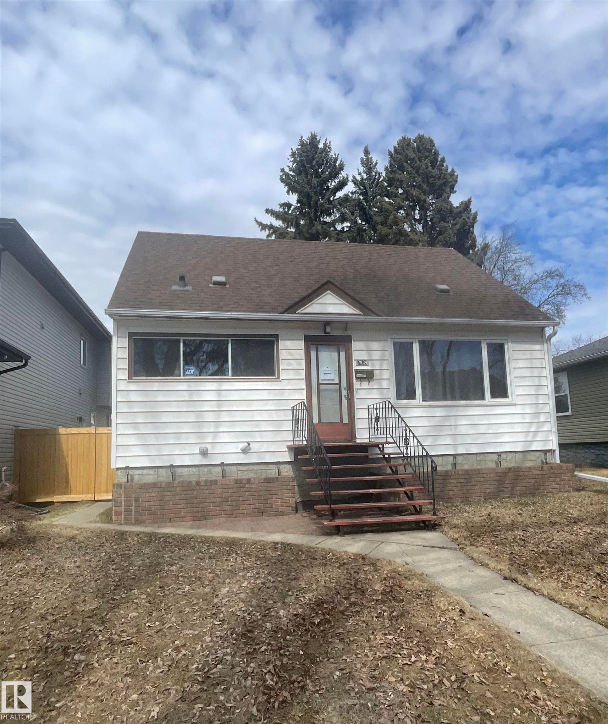 The property features a white exterior, a brown roof, and a front entry with steps and a metal handrail - 7934 81 Avenue, Edmonton, AB