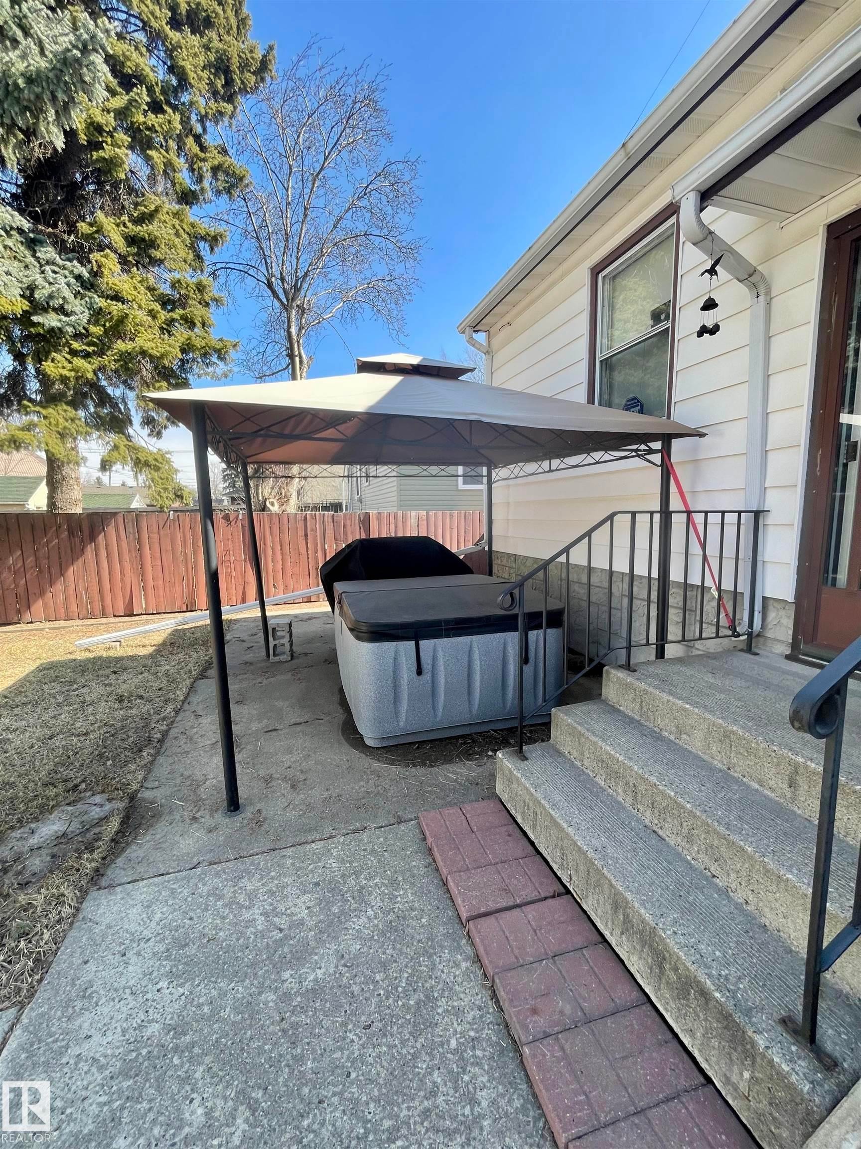 The property features a concrete patio area with a gazebo, a hot tub, and exterior stairs with a metal handrail - 7934 81 Avenue, Edmonton, AB