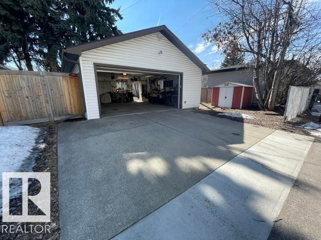 The property features a detached garage with an open garage door, a concrete driveway, and a red and white shed - 7934 81 Avenue, Edmonton, AB