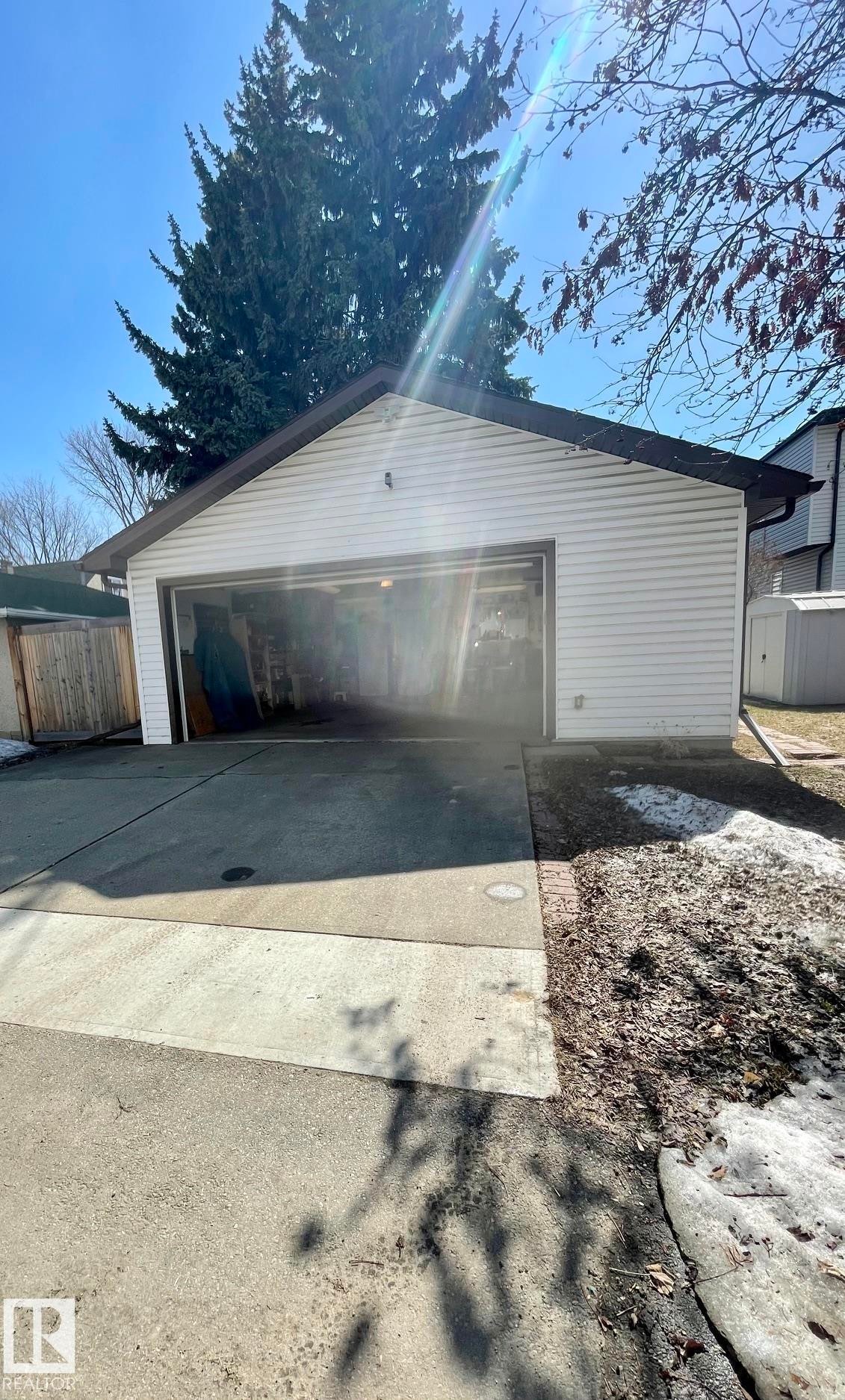 Detached garage with a brown roof and white siding, featuring a partially open door, and a concrete driveway - 7934 81 Avenue, Edmonton, AB