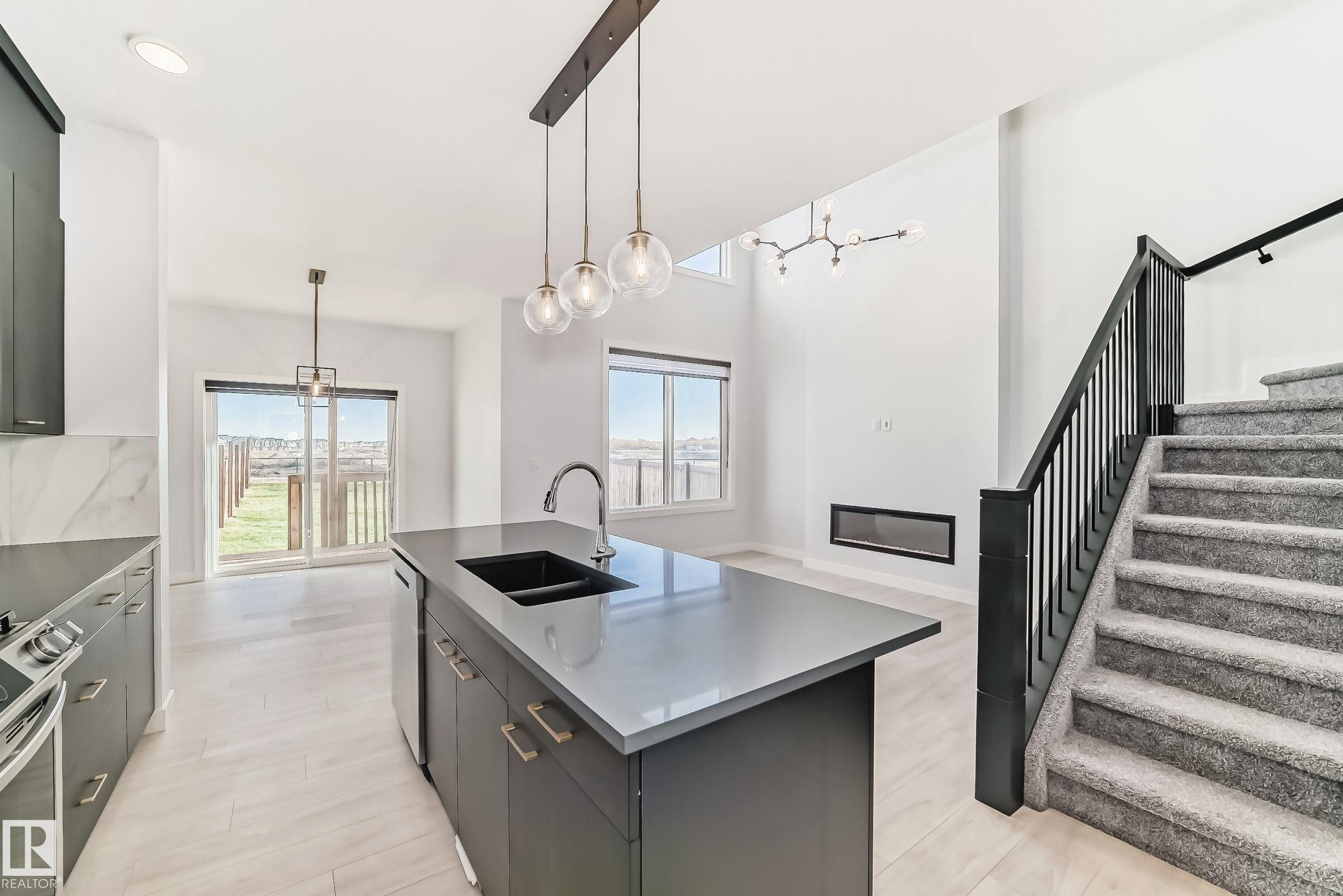 The property features a kitchen island with a sink and pendant lighting, leading to a dining area with sliding glass doors opening to a fenced yard - 9411 Pear Crescent, Edmonton, AB - Indoor Photo Showing Kitchen With Double Sink With Upgraded Kitchen