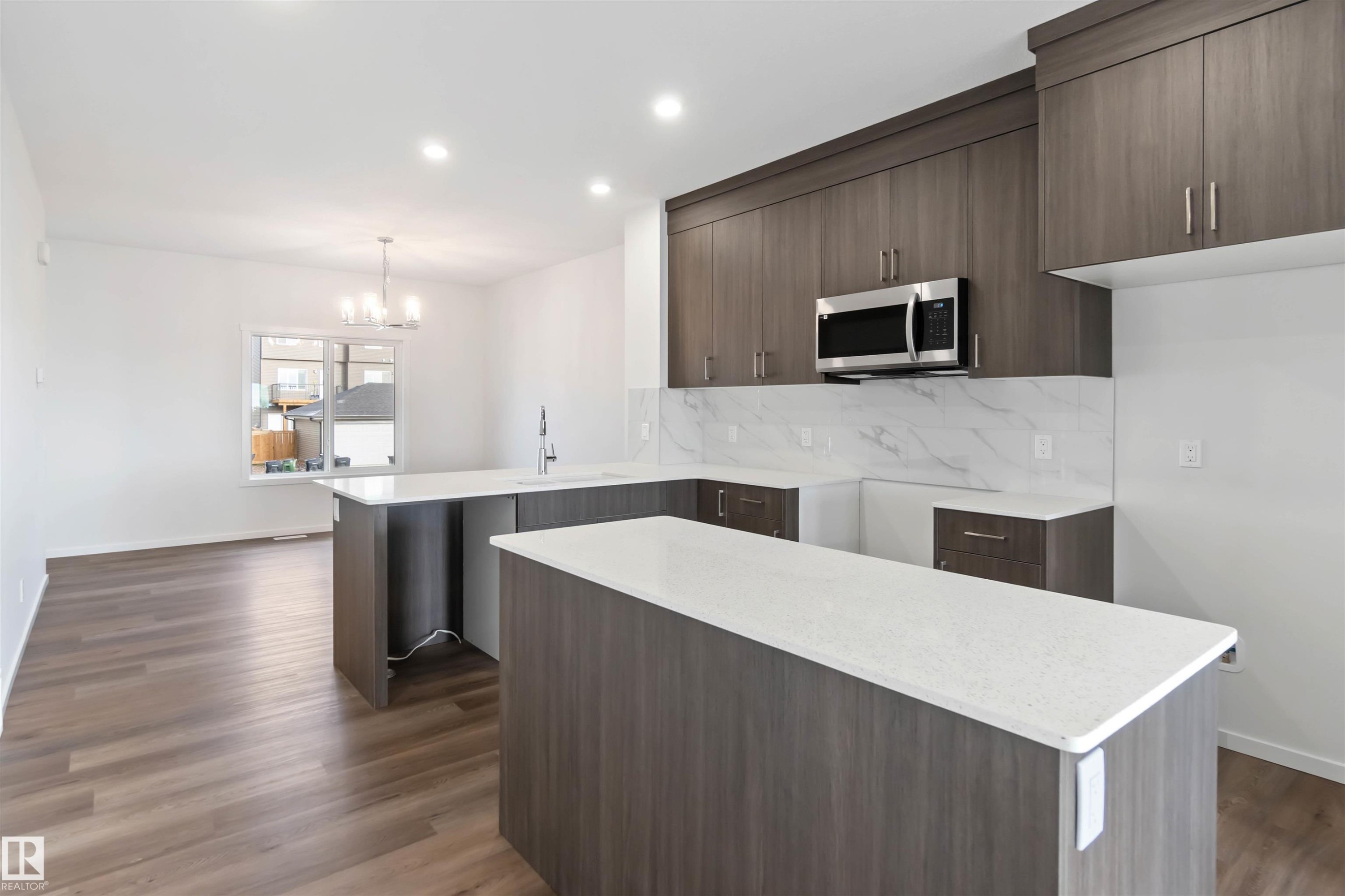 Kitchen featuring dark wood cabinetry, light countertops, a stainless steel microwave, and white tiled backsplash - 5452 Hawthorn Run, Edmonton, AB - Indoor Photo Showing Kitchen With Upgraded Kitchen