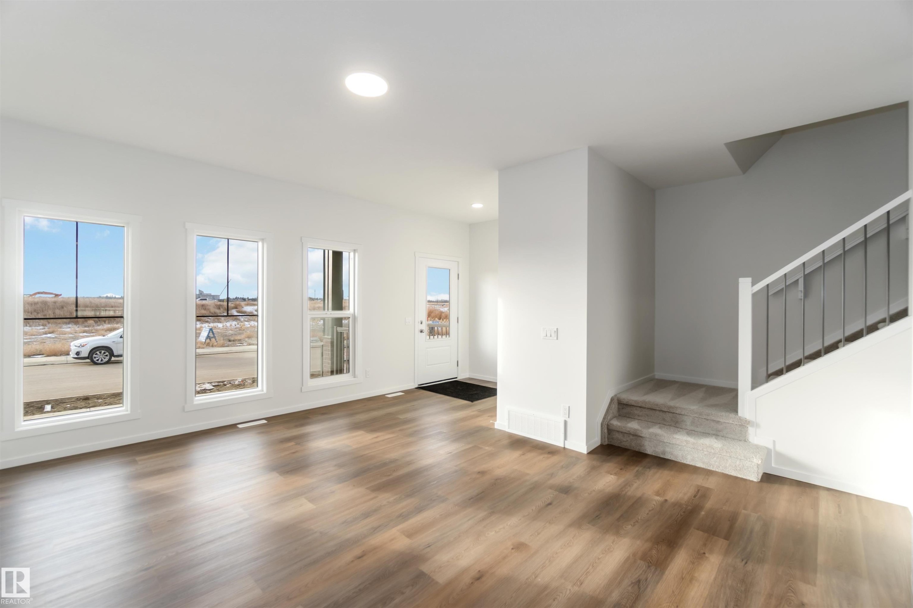 Bright and airy interior featuring durable LVP flooring, multiple large windows, and a carpeted staircase with a modern railing - 5452 Hawthorn Run, Edmonton, AB - Indoor
