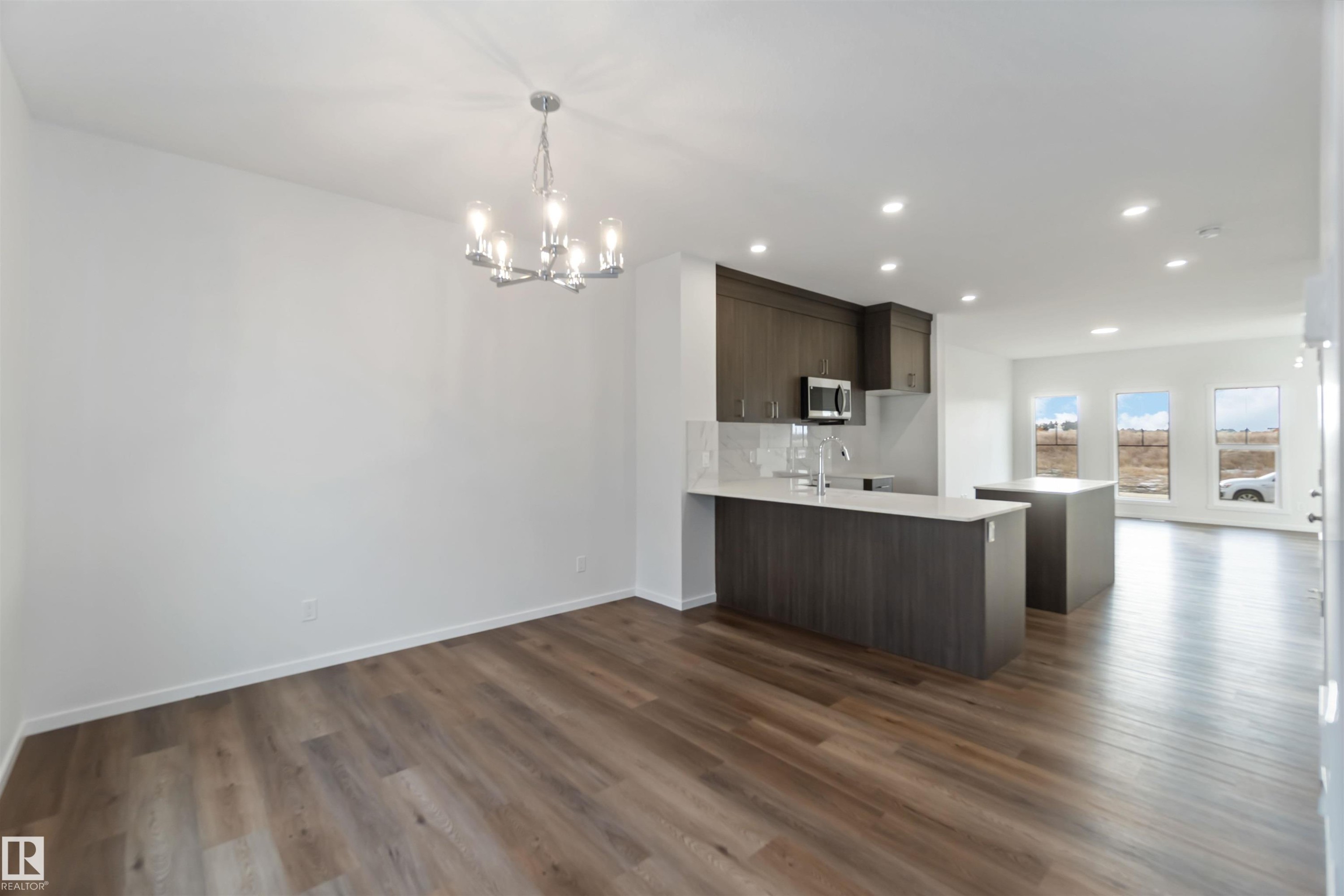 The property features an open-concept living area with hardwood flooring, a modern kitchen with dark cabinetry and light countertops, a kitchen island, and recessed lighting - 5452 Hawthorn Run, Edmonton, AB - Indoor Photo Showing Kitchen
