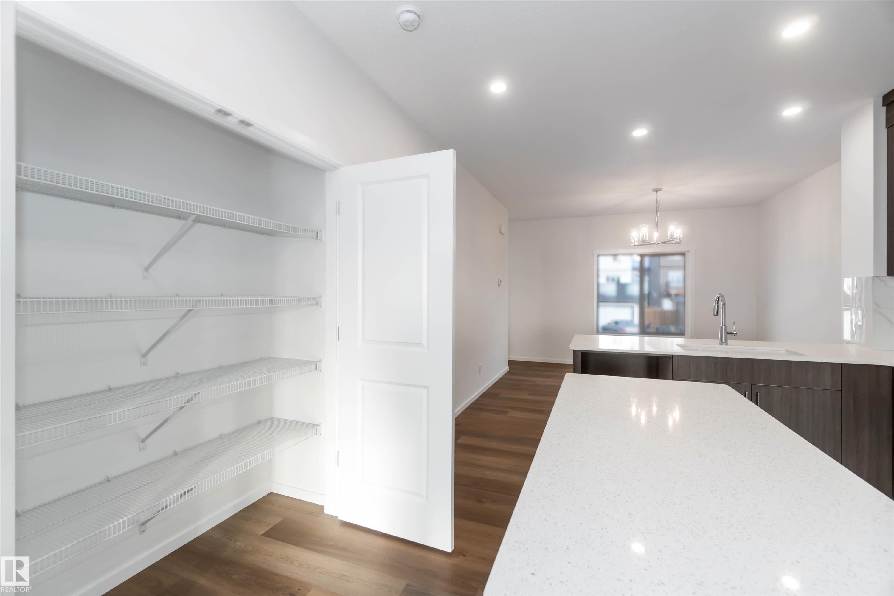 The kitchen features a white countertop island, a sink with a stainless steel faucet, and dark wood cabinetry - 5452 Hawthorn Run, Edmonton, AB - Indoor