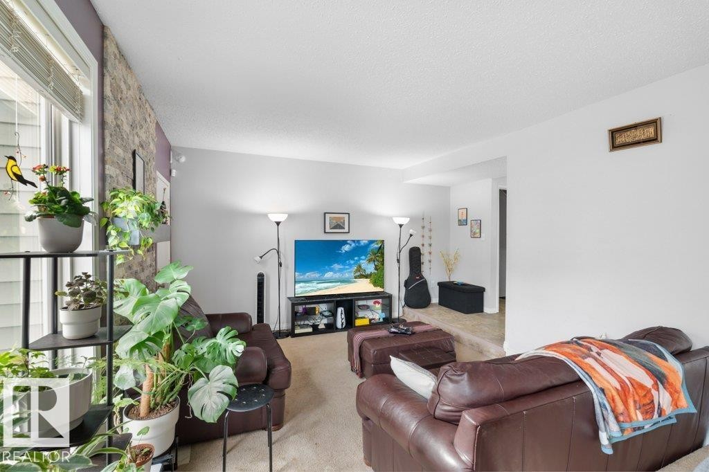 Inviting living area featuring a large window with blinds, a textured accent wall, and carpeted flooring - 638 Saddleback Road, Edmonton, AB - Indoor
