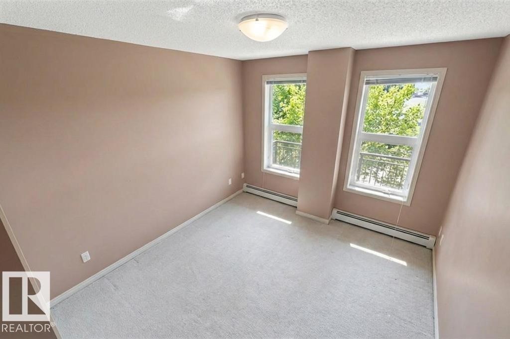 This room features two windows with views of abundant greenery, carpeted flooring, and a ceiling light fixture - 1-204 4245 139 Avenue, Edmonton, AB - Indoor Photo Showing Other Room