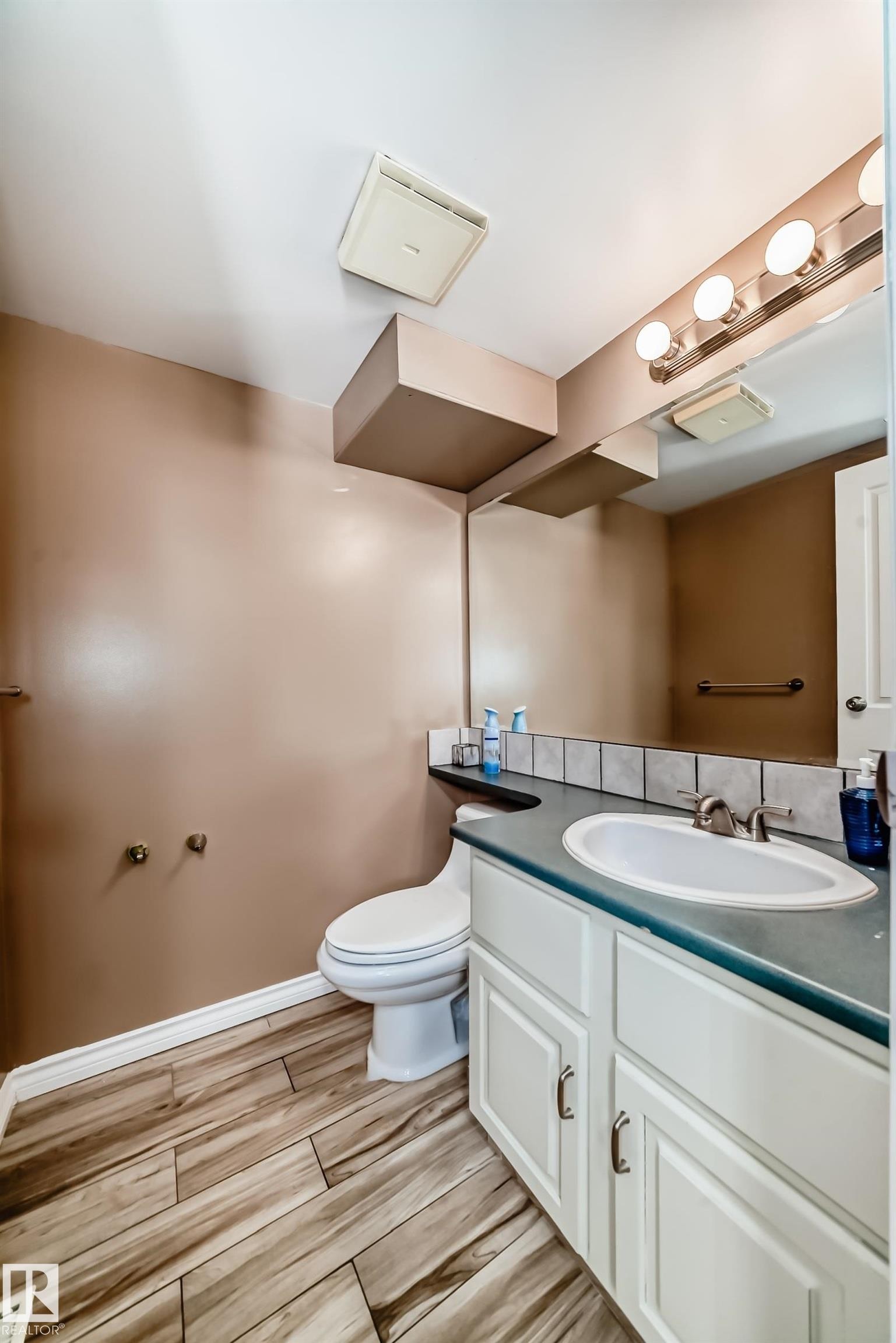 Bathroom featuring wood-look tile flooring, a white vanity with a countertop sink, a large wall mirror, and a wall-mounted light fixture - 597 Millbourne Road E, Edmonton, AB - Indoor Photo Showing Bathroom
