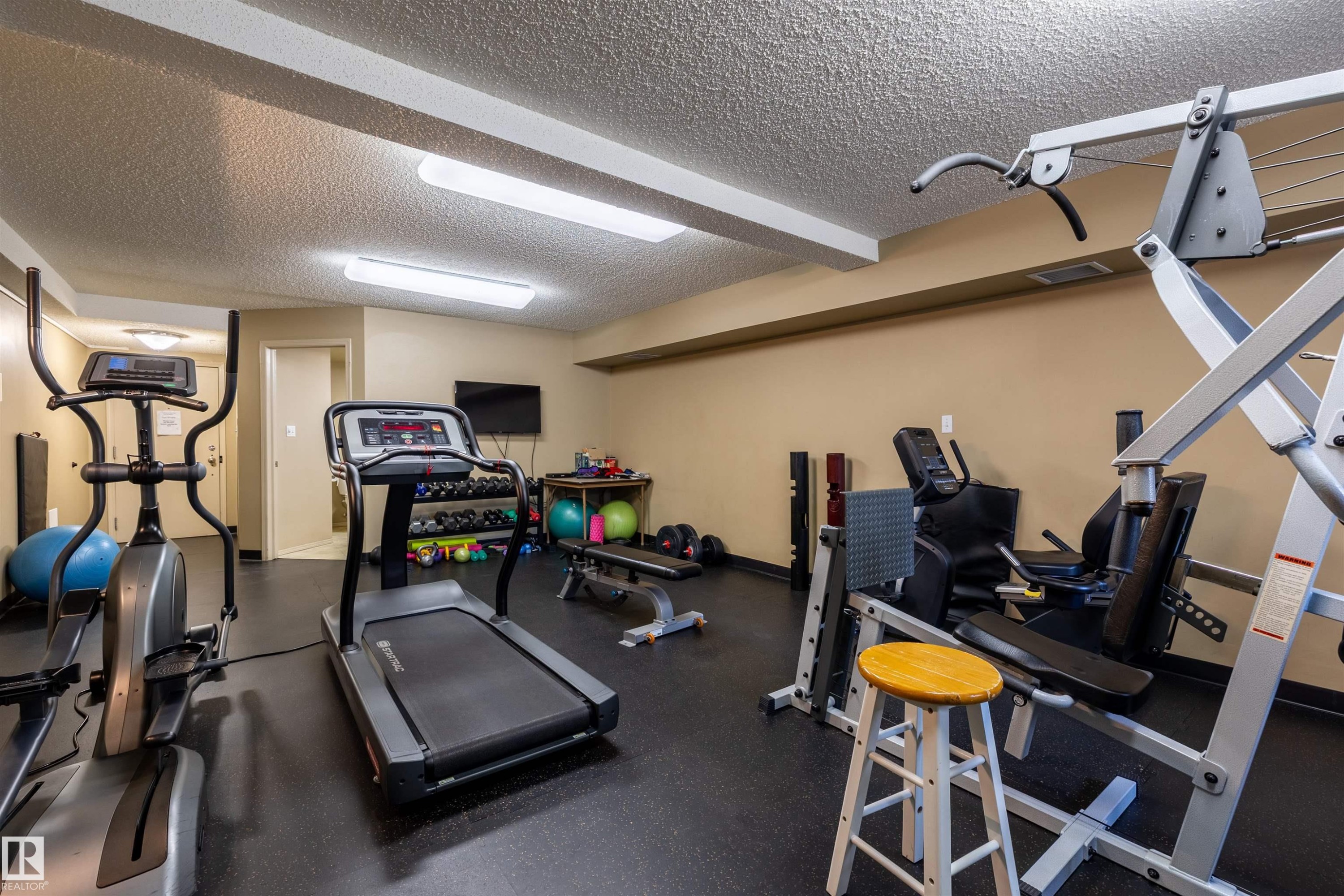 The property features a dedicated fitness area with gym equipment, including a treadmill, an elliptical machine, and weight training apparatus - #515 10311 111 St Nw, Edmonton, AB - Indoor Photo Showing Gym Room