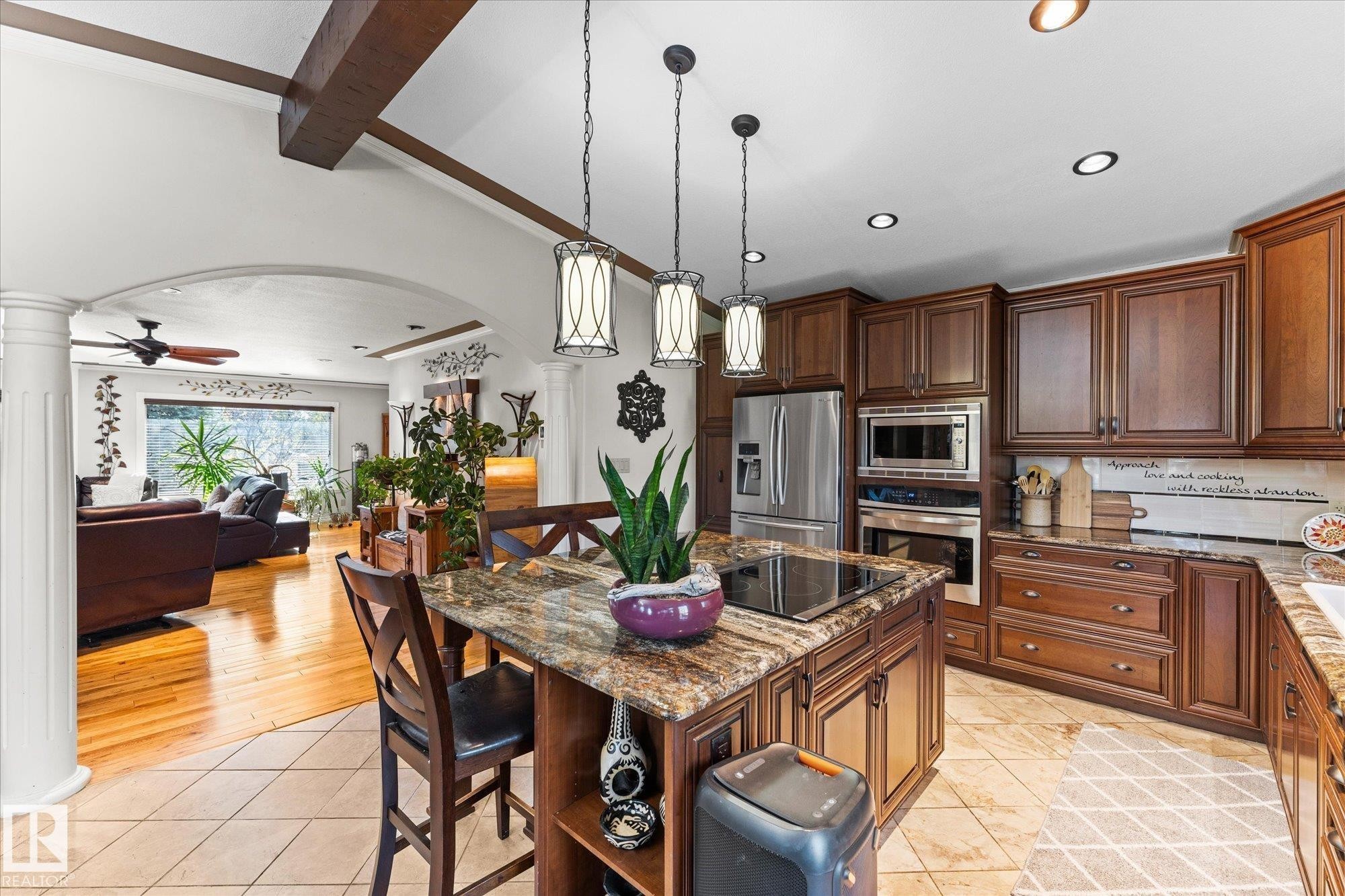 The kitchen features a central island with a built-in cooktop and granite countertops, complemented by rich wooden cabinetry and stainless steel appliances - 11124 110A Avenue, Edmonton, AB - Indoor Photo Showing Kitchen With Upgraded Kitchen