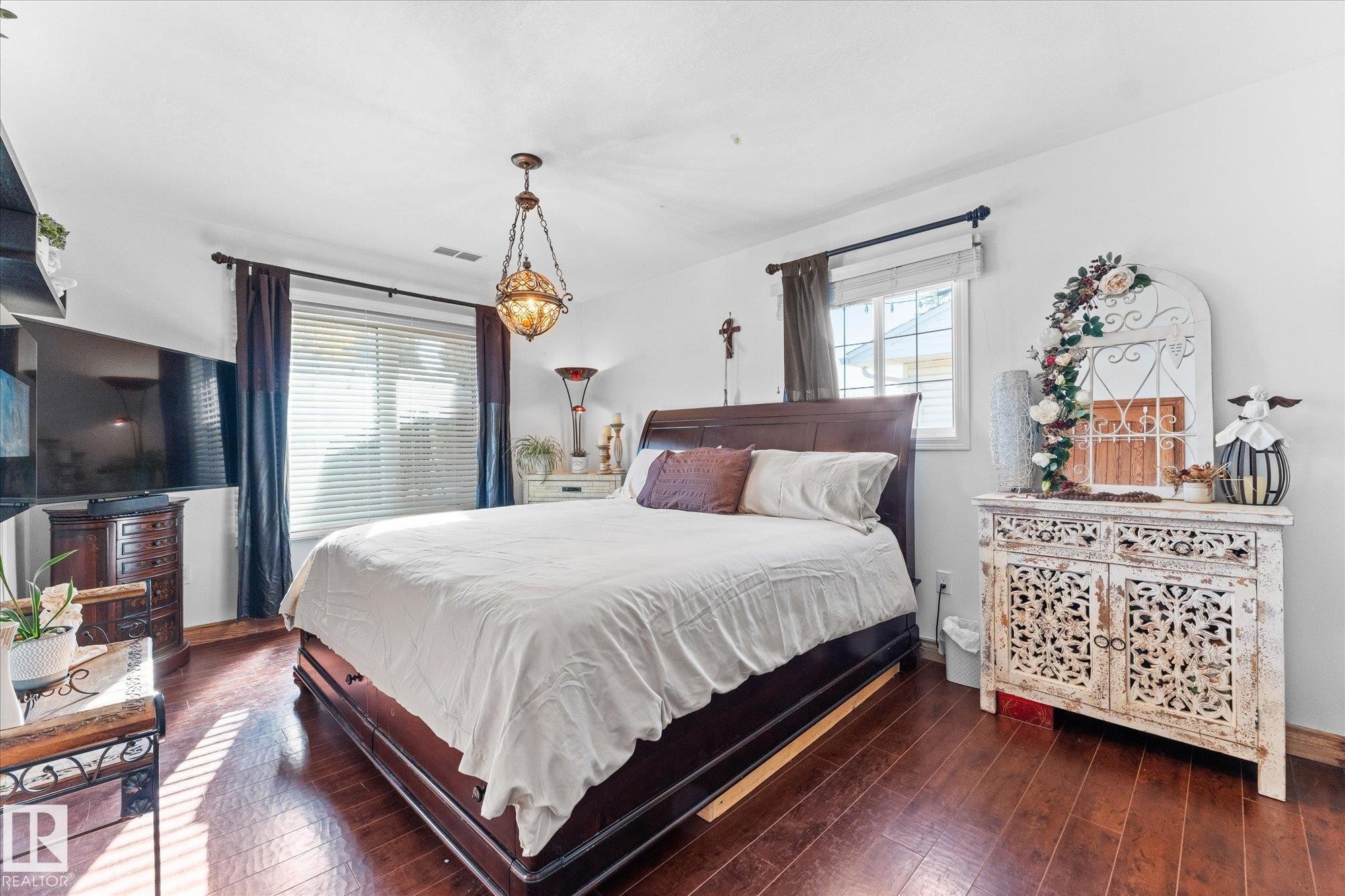 This room features rich wood flooring, a window with blinds and dark curtains, and a decorative overhead light fixture - 11124 110A Avenue, Edmonton, AB - Indoor Photo Showing Bedroom