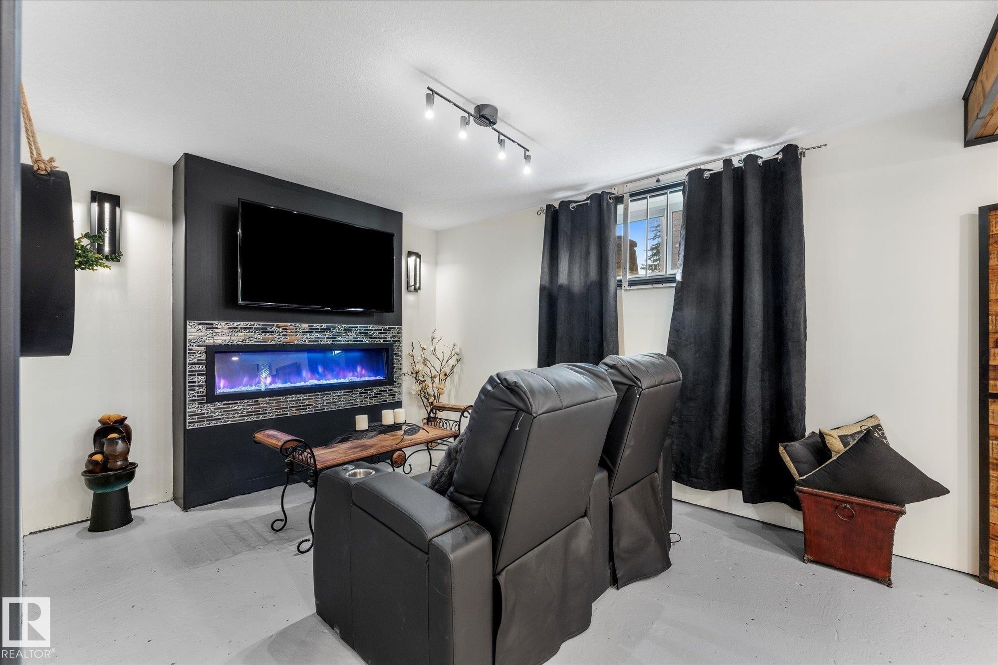 The room features a modern wall-mounted fireplace with blue lighting, a wall-mounted television, and track lighting on the ceiling - 11124 110A Avenue, Edmonton, AB - Indoor