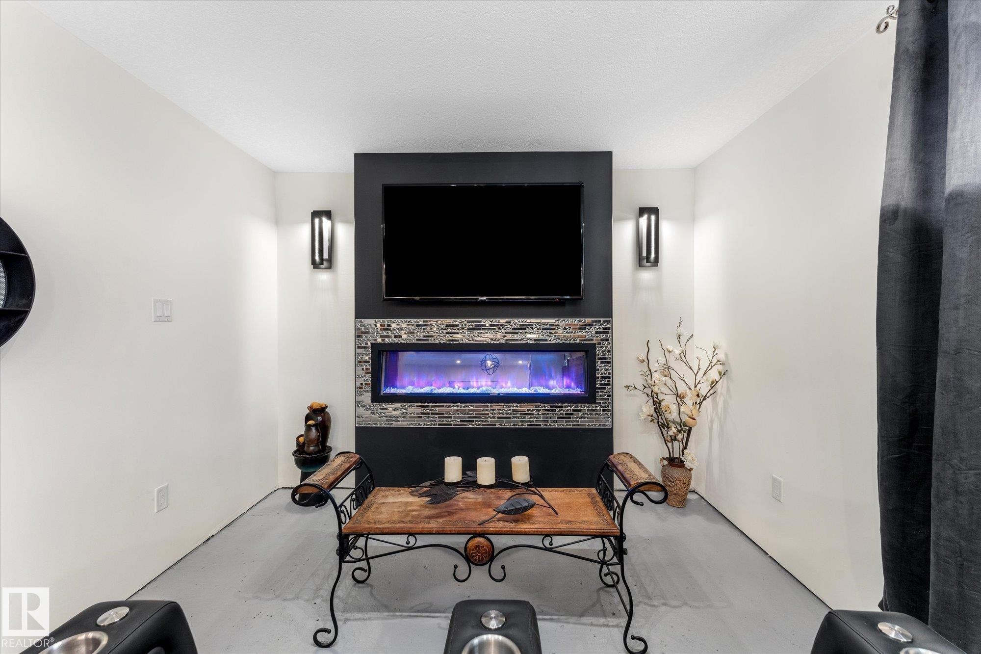 Living area featuring a wall-mounted television above an electric fireplace, set within a dark accent wall with decorative tile work - 11124 110A Avenue, Edmonton, AB - Indoor