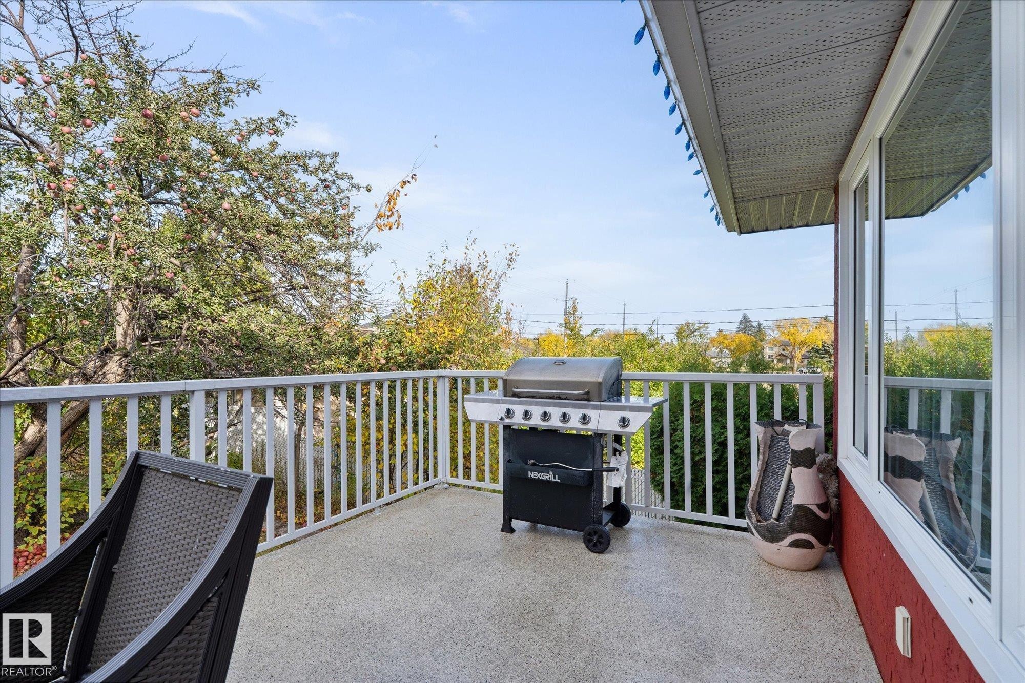 The property features an outdoor deck with a white railing, providing views of mature trees - 11124 110A Avenue, Edmonton, AB - Outdoor With Deck Patio Veranda With Exterior