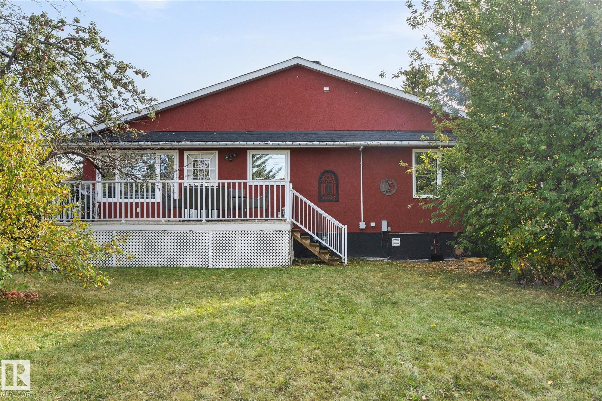 The property features an extensive backyard with a lawn, a red exterior, and a white deck with railings and stairs - 11124 110A Avenue, Edmonton, AB - Outdoor With Deck Patio Veranda