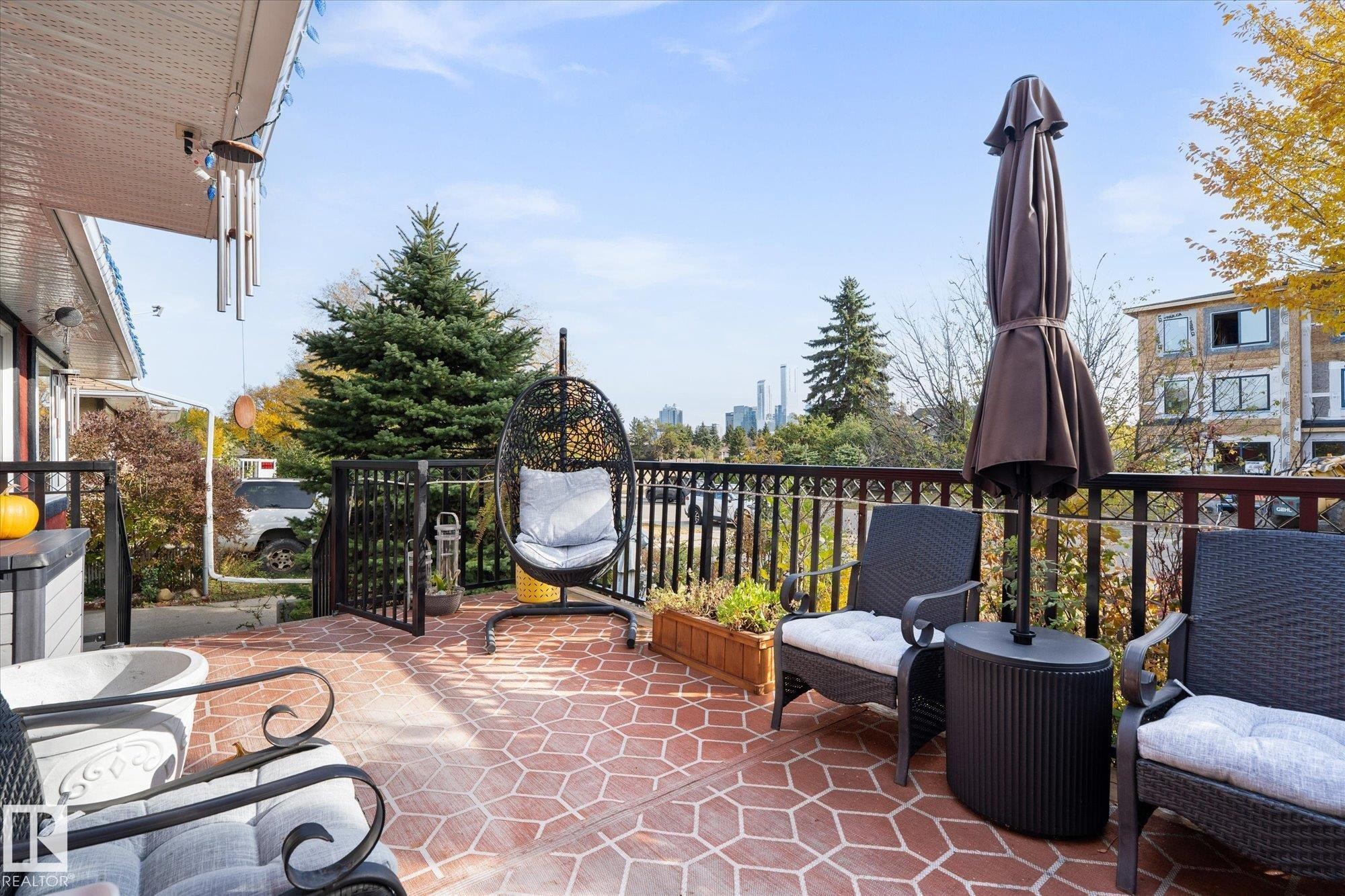 The property features an expansive outdoor patio with a red patterned surface, black metal railings, and views of city buildings in the distance - 11124 110A Avenue, Edmonton, AB - Outdoor With Exterior