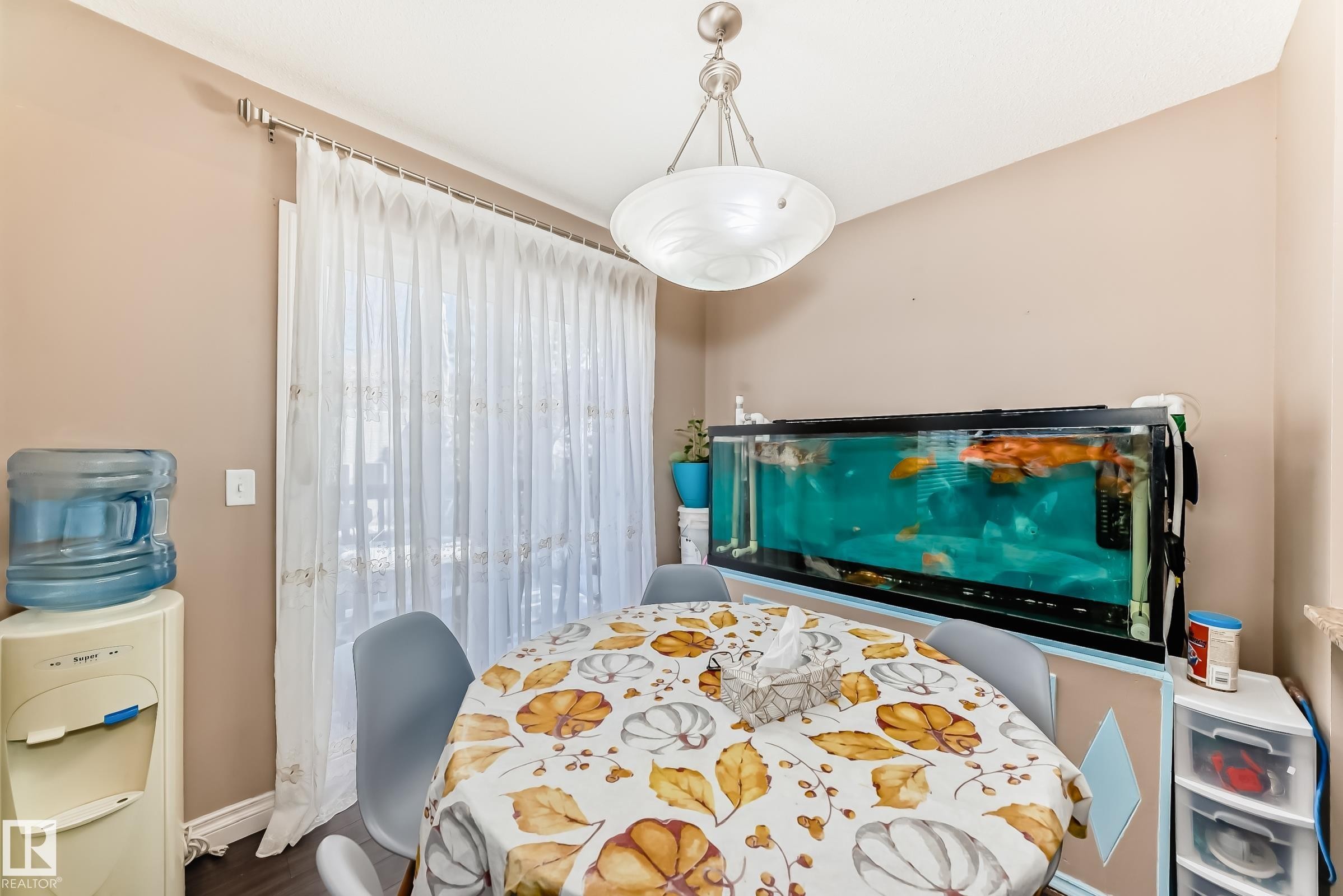 This room features neutral-toned walls, a decorative overhead light fixture, and a large window with sheer white curtains - 23 445 Brintnell Boulevard Nw, Edmonton, AB - Indoor Photo Showing Other Room