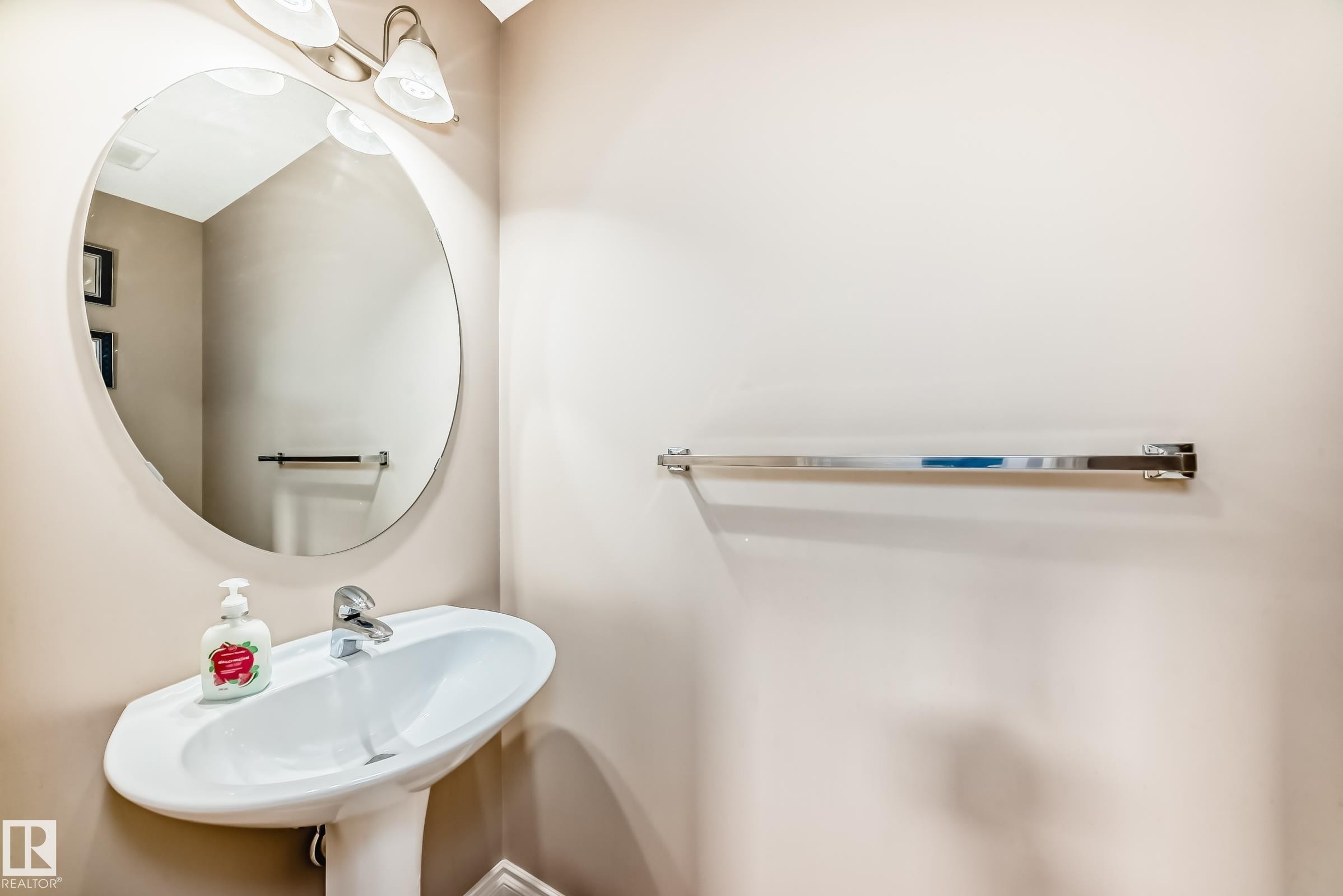 This bathroom features a pedestal sink with a chrome faucet, a large oval mirror, and a wall-mounted light fixture with two sconces - 23 445 Brintnell Boulevard Nw, Edmonton, AB - Indoor Photo Showing Bathroom