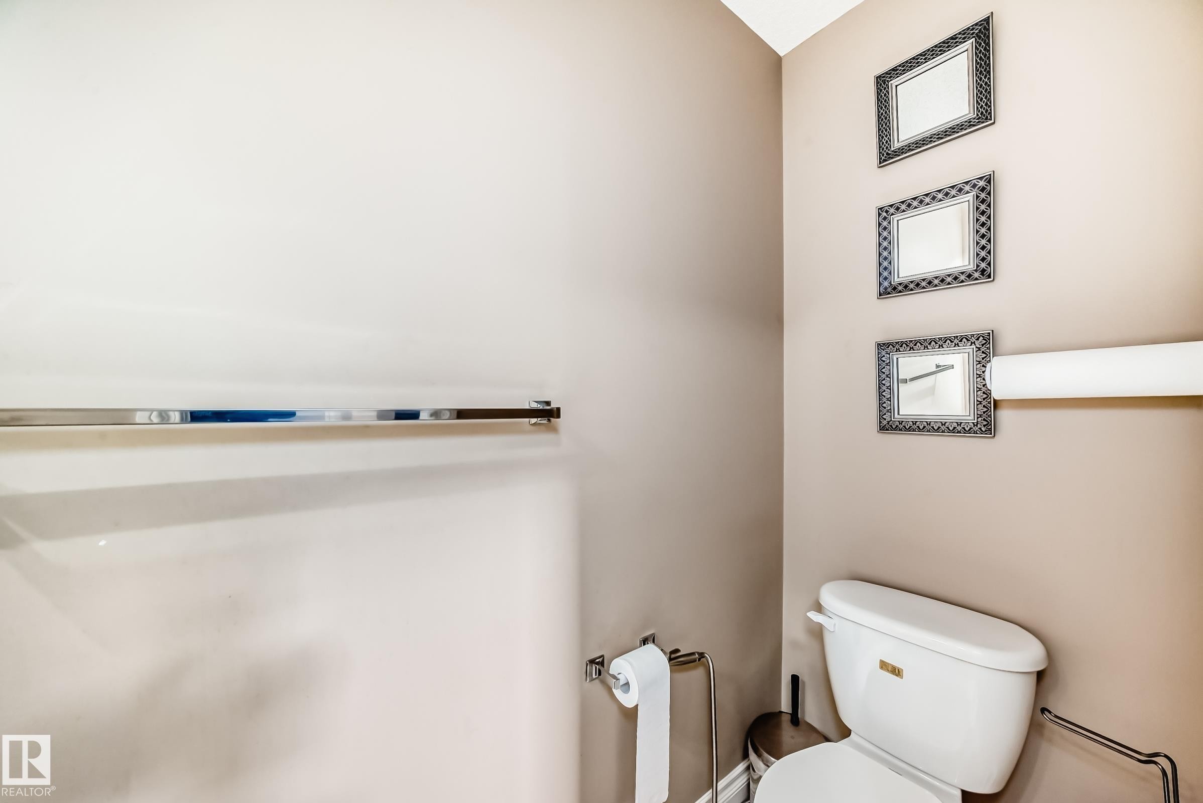 Bathroom featuring a white toilet with a beige tank lid, a chrome towel bar, and decorative framed mirrors - 23 445 Brintnell Boulevard Nw, Edmonton, AB - Indoor Photo Showing Bathroom