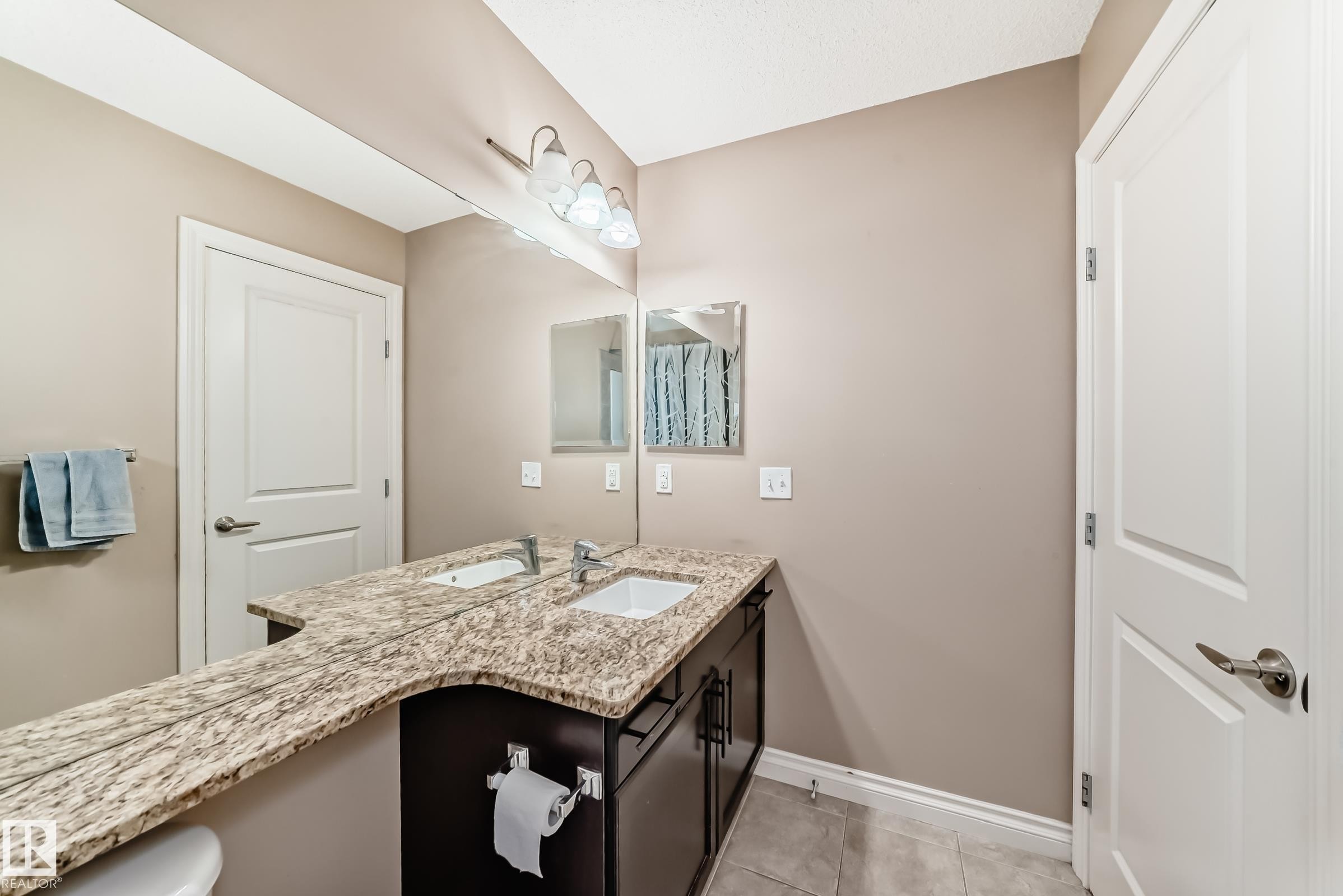The bathroom features a double vanity with a speckled countertop, integrated sinks, and dark wood cabinetry - 23 445 Brintnell Boulevard Nw, Edmonton, AB - Indoor Photo Showing Bathroom