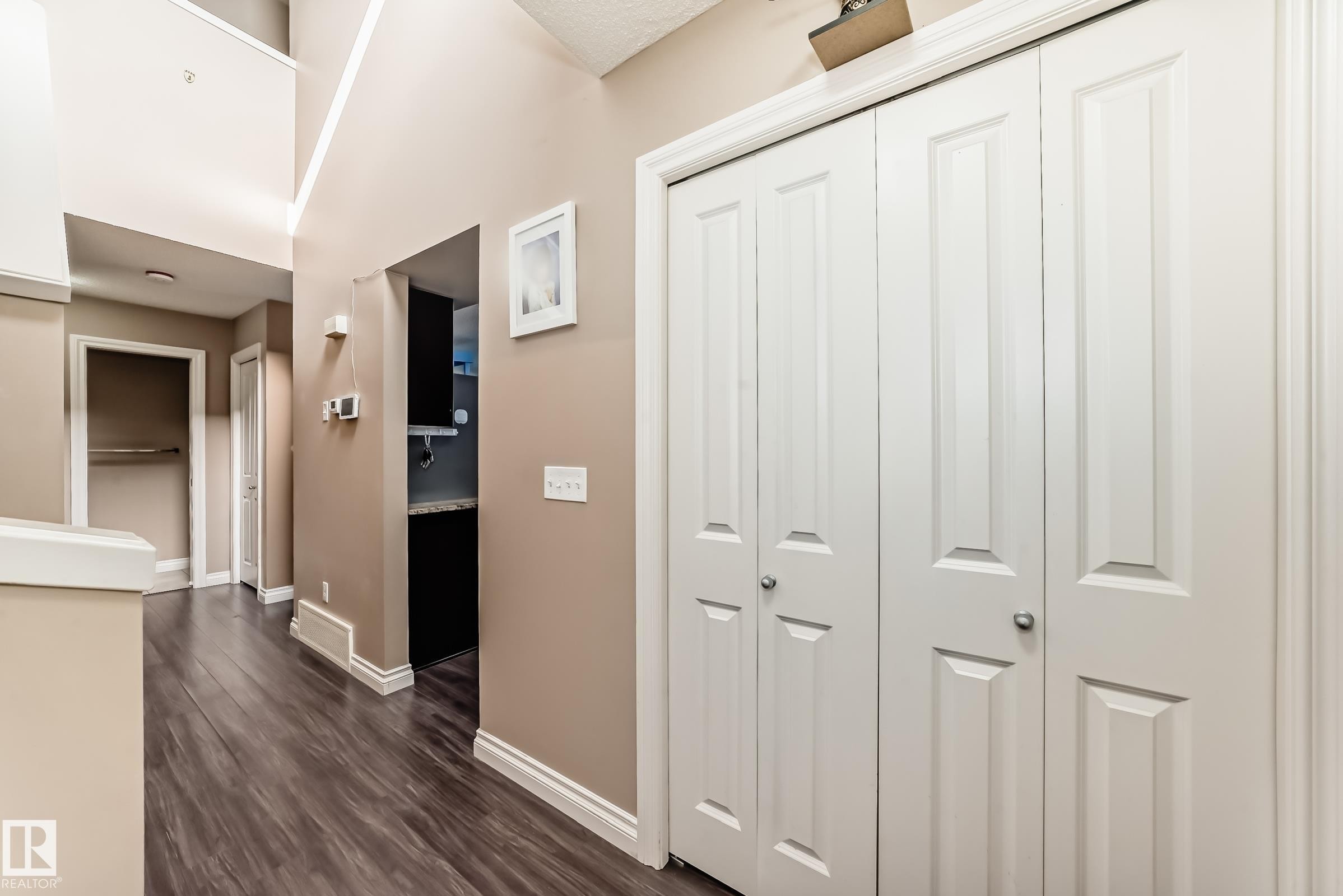 The property features neutral-toned walls, dark wood-style flooring, and white trim throughout the hallway - 23 445 Brintnell Boulevard Nw, Edmonton, AB - Indoor Photo Showing Other Room
