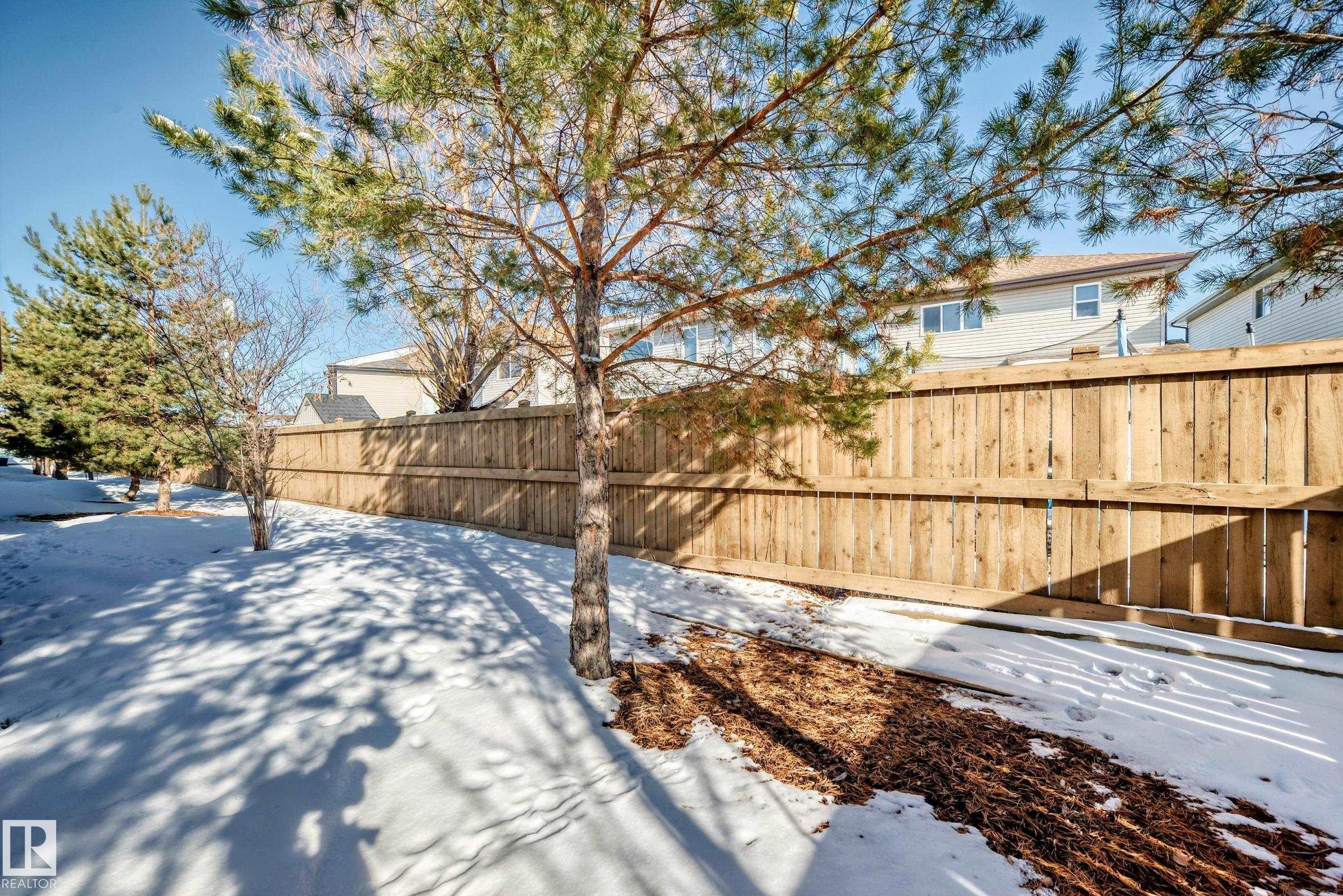 The property features a wood fence and mature trees - 23 445 Brintnell Boulevard Nw, Edmonton, AB - Outdoor