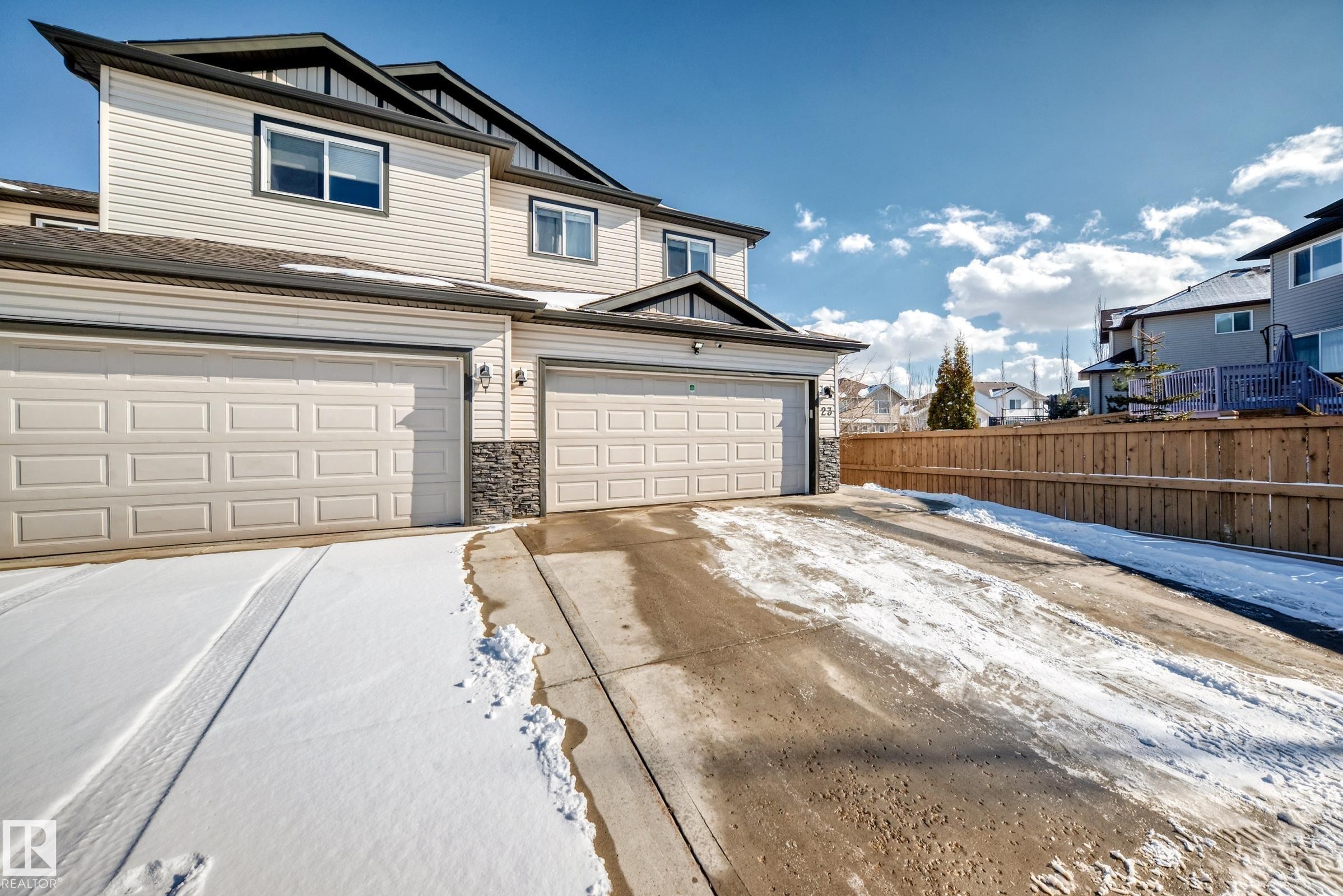 Exterior view of the property featuring a two-story design, light-colored siding, and a double garage with sectional doors - 23 445 Brintnell Boulevard Nw, Edmonton, AB - Outdoor