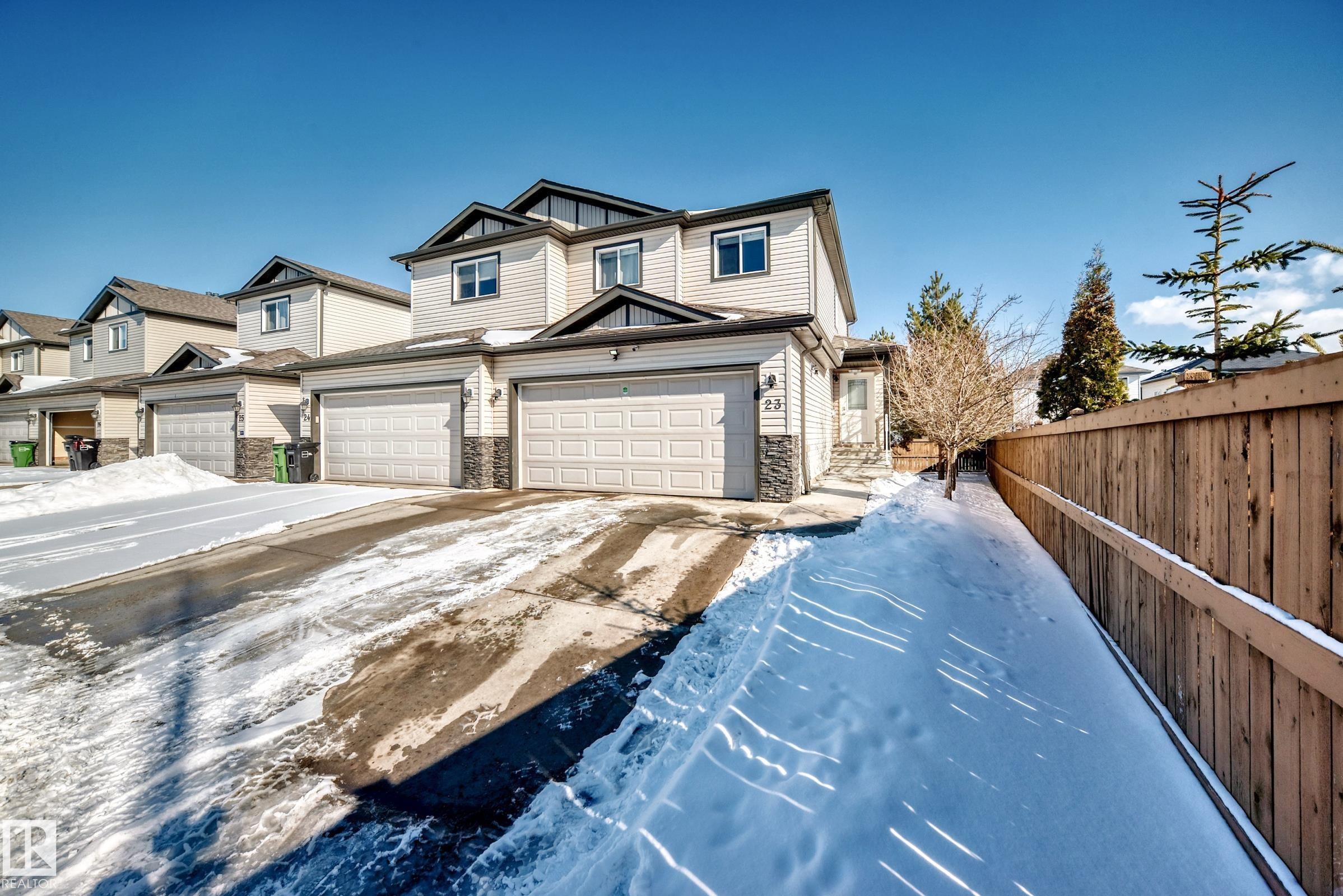 This property features light-colored siding with dark trim accents and an attached garage with a stone facade detail - 23 445 Brintnell Boulevard Nw, Edmonton, AB - Outdoor