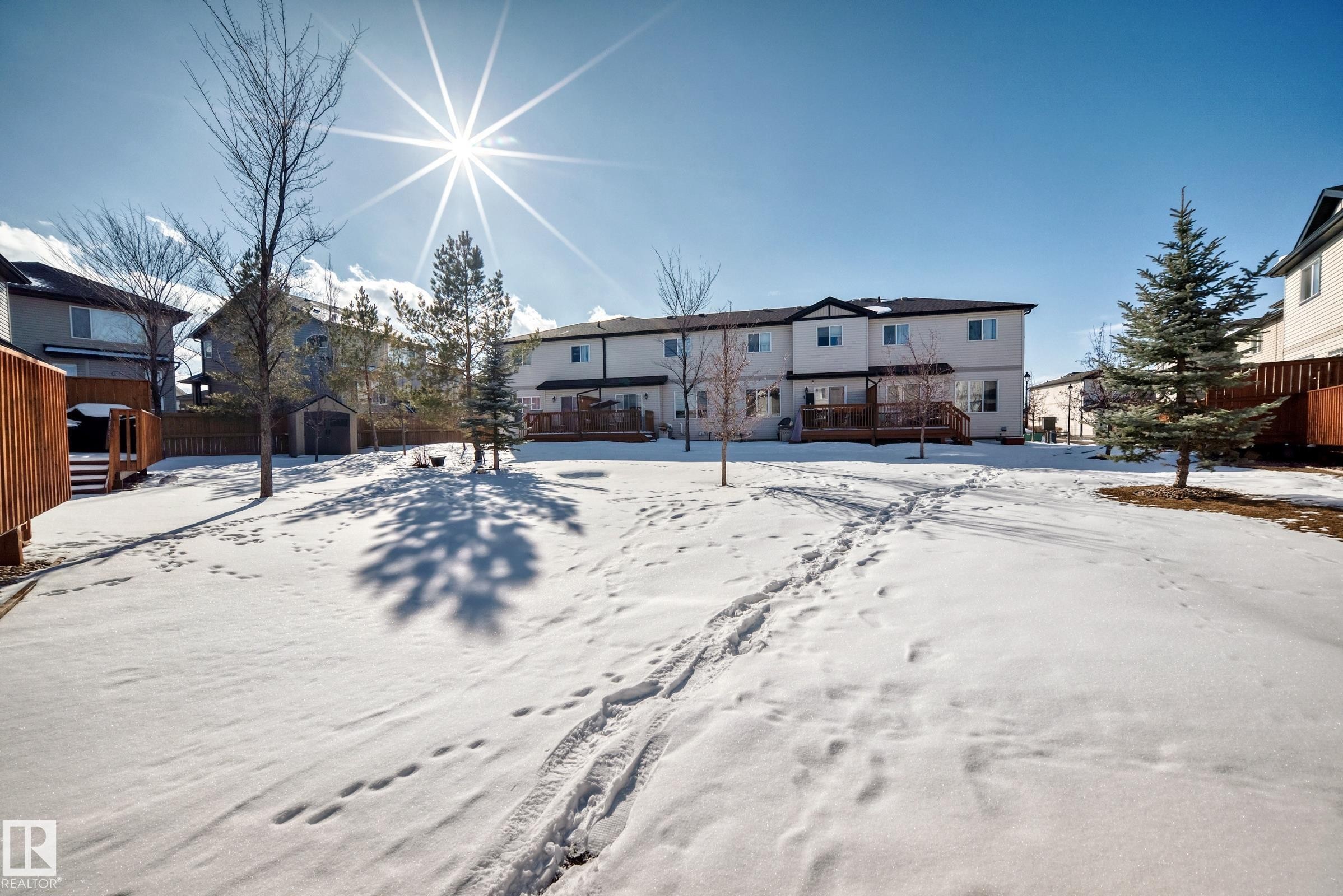 Expansive backyard with a snow-covered lawn, mature trees, and a wooden fence - 23 445 Brintnell Boulevard Nw, Edmonton, AB - Outdoor