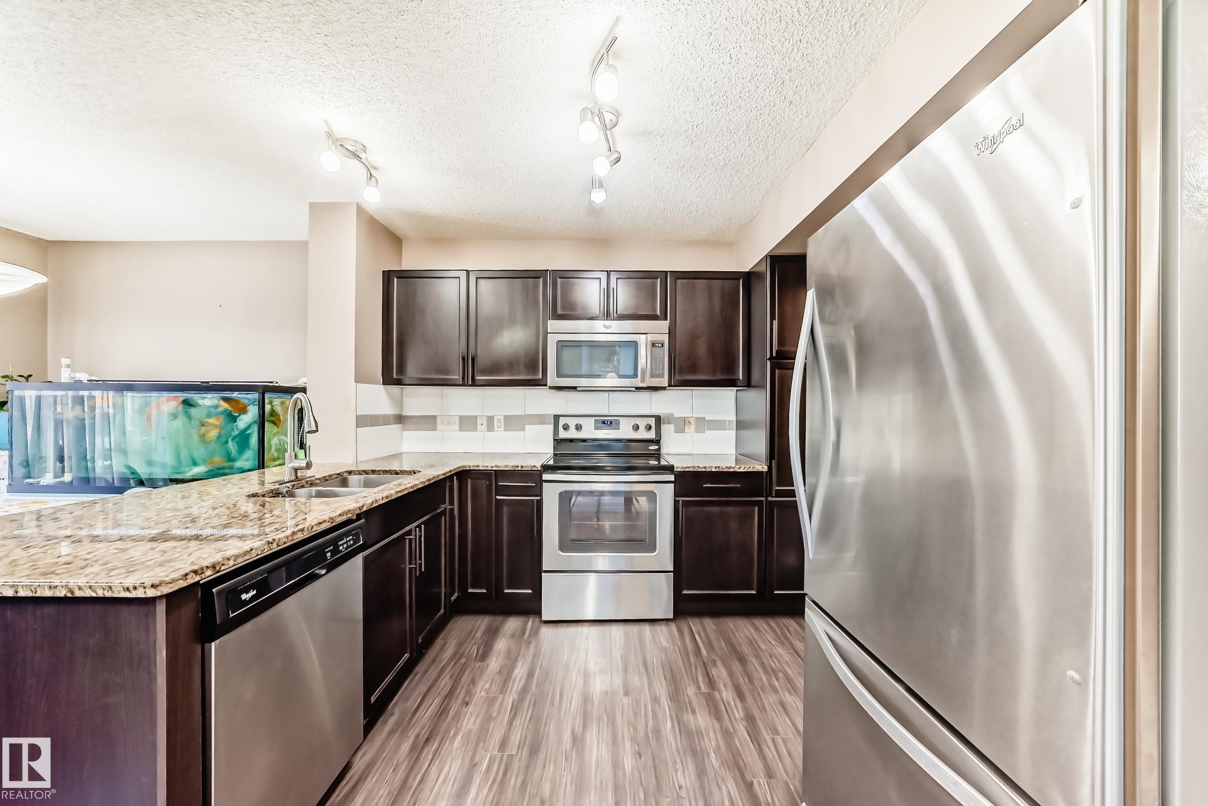 The kitchen features dark wood cabinetry, granite countertops, and stainless steel appliances, including a refrigerator, stove, and microwave - 23 445 Brintnell Boulevard Nw, Edmonton, AB - Indoor Photo Showing Kitchen With Double Sink With Upgraded Kitchen