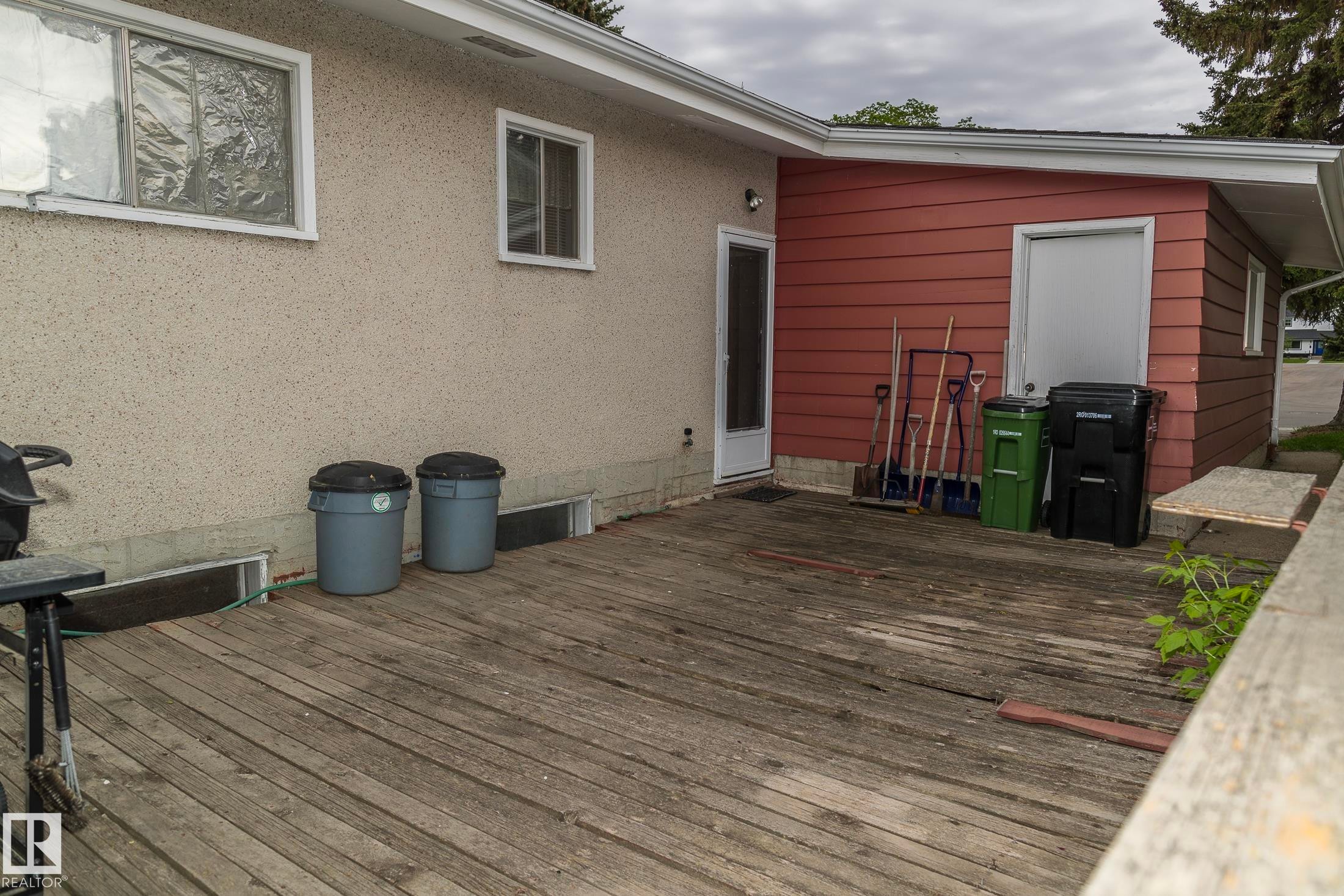 Property exterior featuring a wooden deck, a light-colored stucco wall, and a section with red siding - 10512 55 Avenue, Edmonton, AB - Outdoor With Exterior