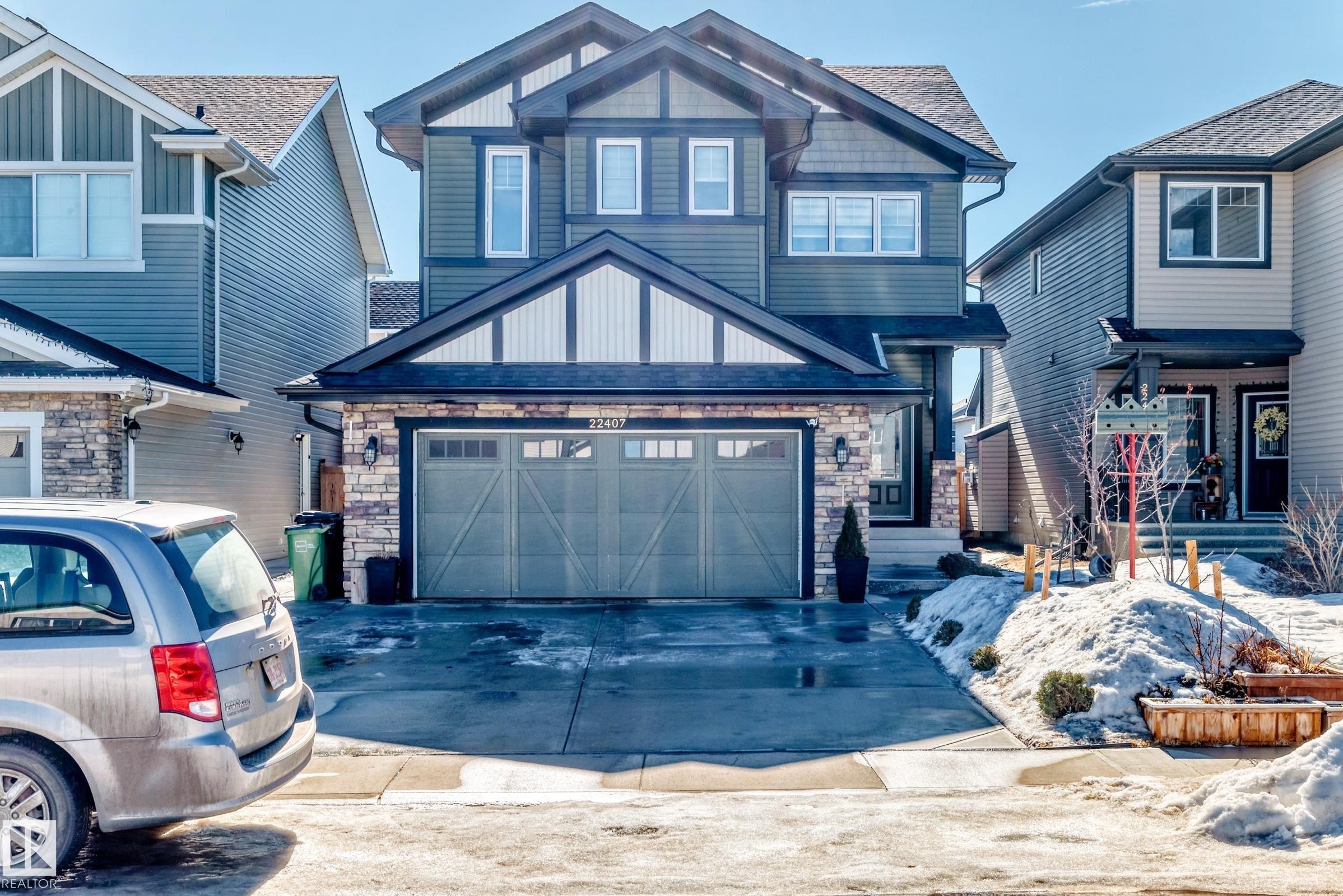 The property features a two-car garage with a paved driveway, stone accents on the facade, and a covered front entrance - 22407 99 Avenue, Edmonton, AB - Outdoor With Facade