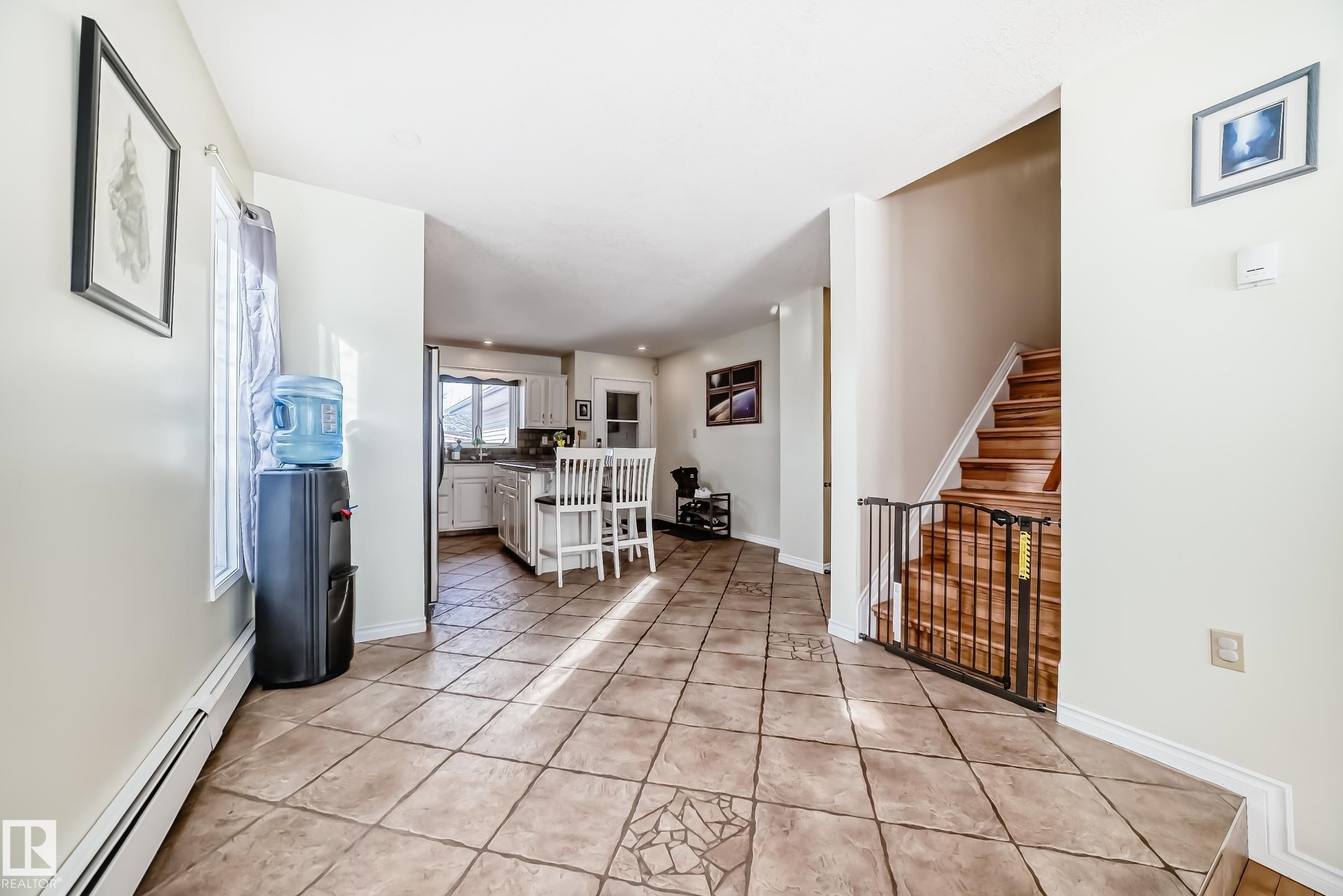 Spacious entryway featuring tiled flooring, a clear view into the kitchen area, and a hardwood staircase with a gate - 16232 100 Street, Edmonton, AB - Indoor Photo Showing Other Room