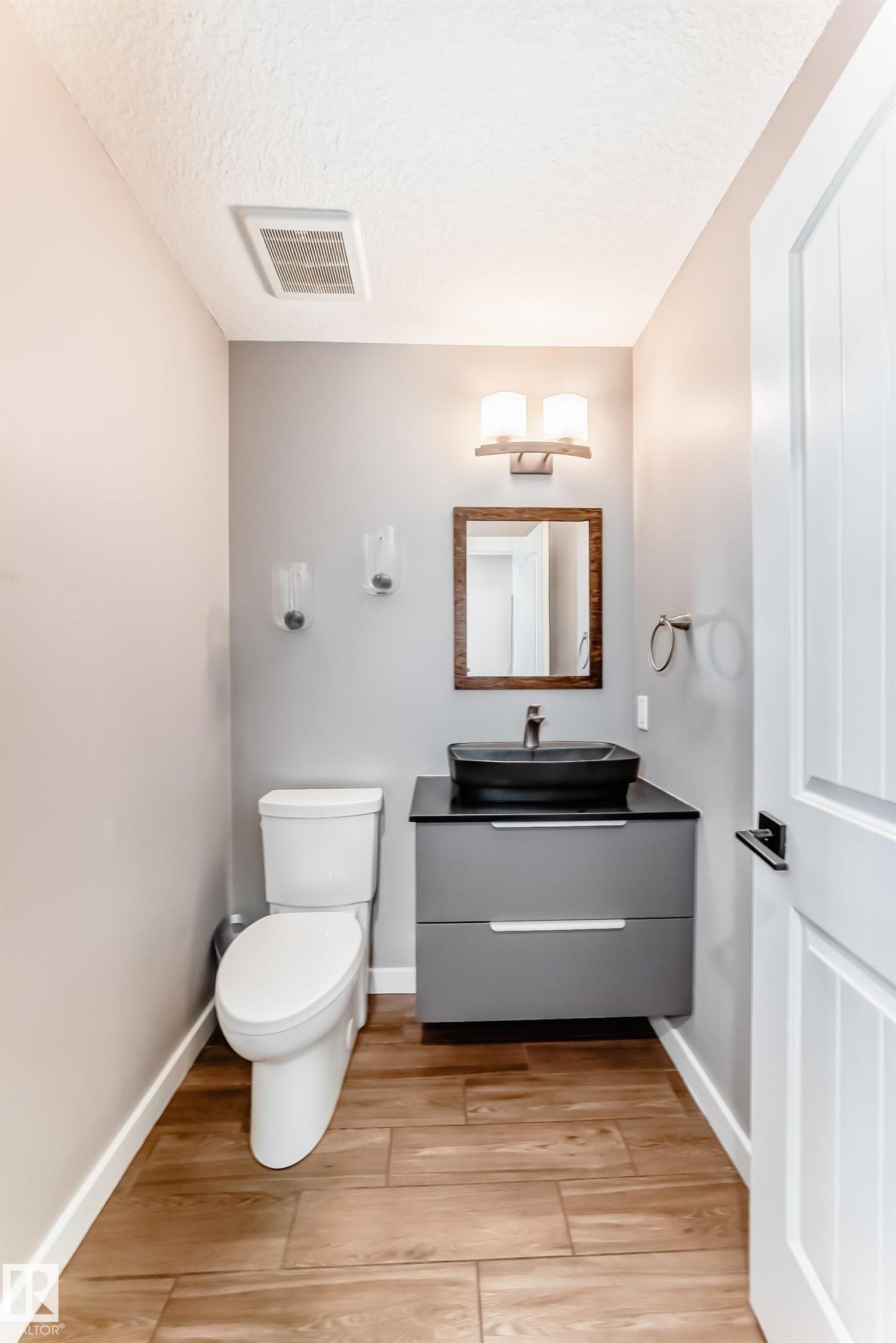 Bathroom featuring wood-look tile flooring, a modern floating vanity with a vessel sink, and a white paneled door - 6303 2 Avenue, Edmonton, AB - Indoor Photo Showing Bathroom