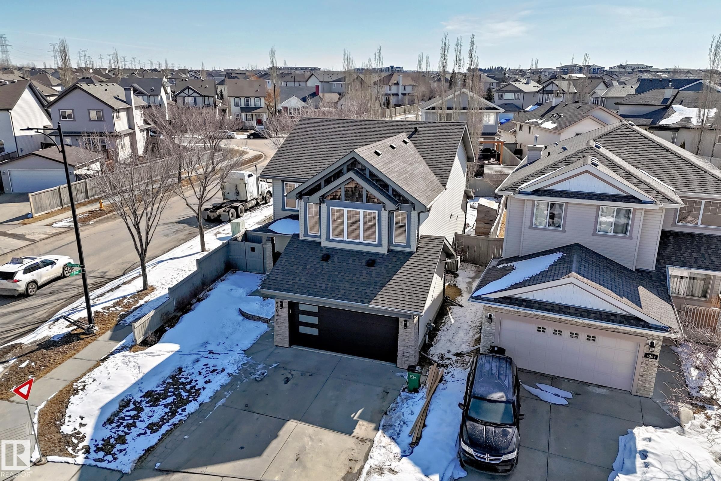 The property features a two-car garage, a paved driveway, and an exterior of light-colored siding and stone accents - 6303 2 Avenue, Edmonton, AB - Outdoor