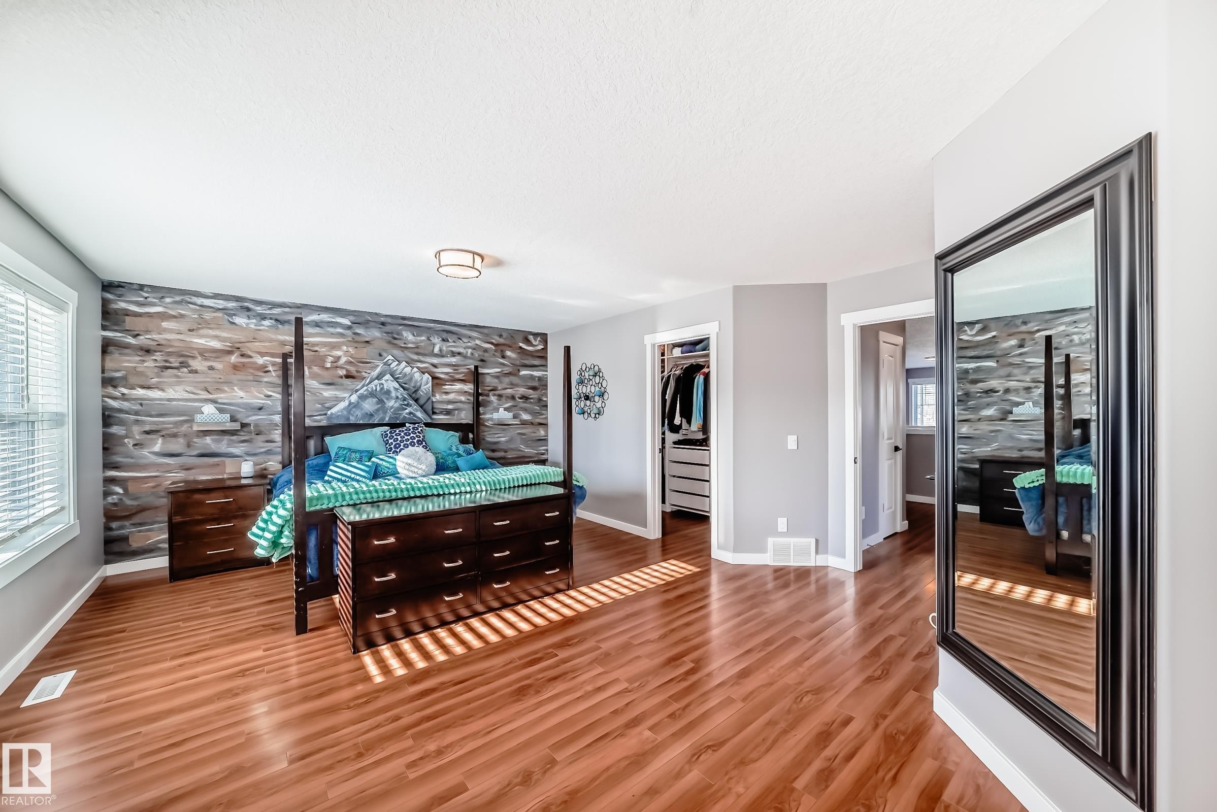 Bedroom featuring hardwood floors, a prominent wood-paneled accent wall, a window with blinds, and an open closet area - 6303 2 Avenue, Edmonton, AB - Indoor