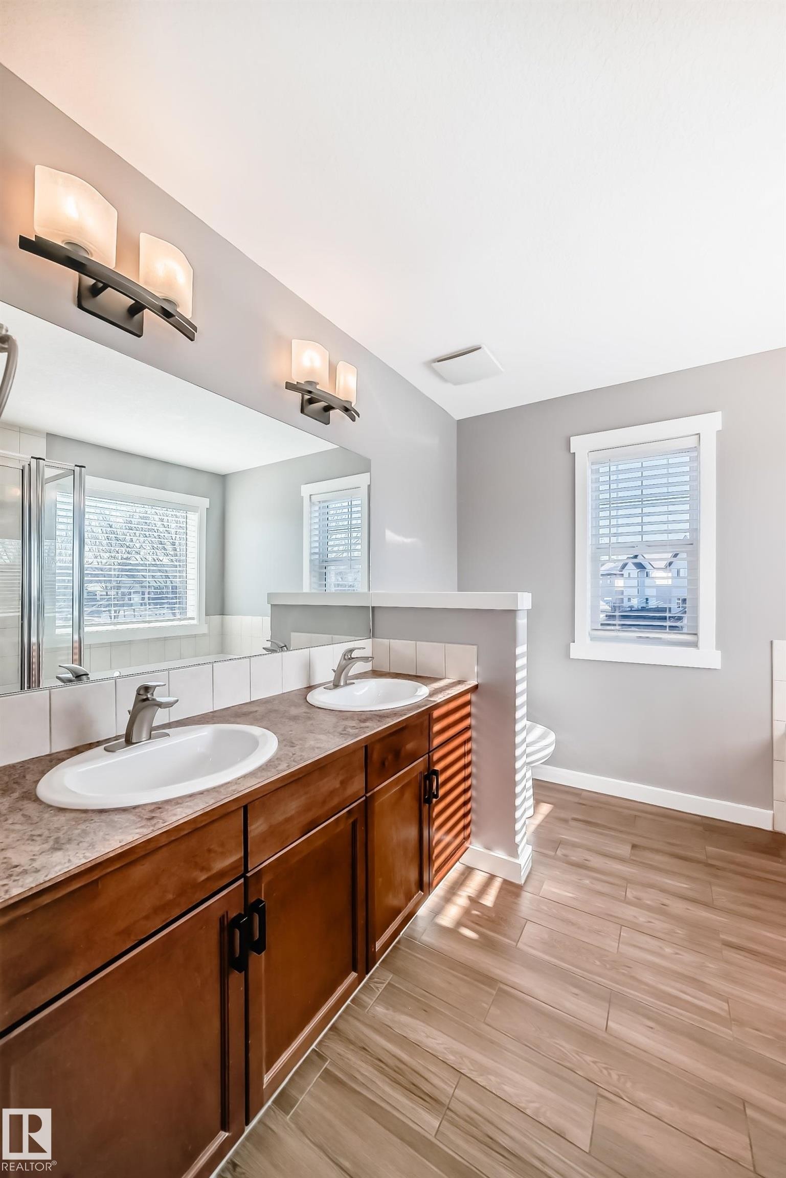 This bathroom features a double vanity with two sinks and undermount cabinetry, a large mirror, and tiled flooring - 6303 2 Avenue, Edmonton, AB - Indoor Photo Showing Bathroom