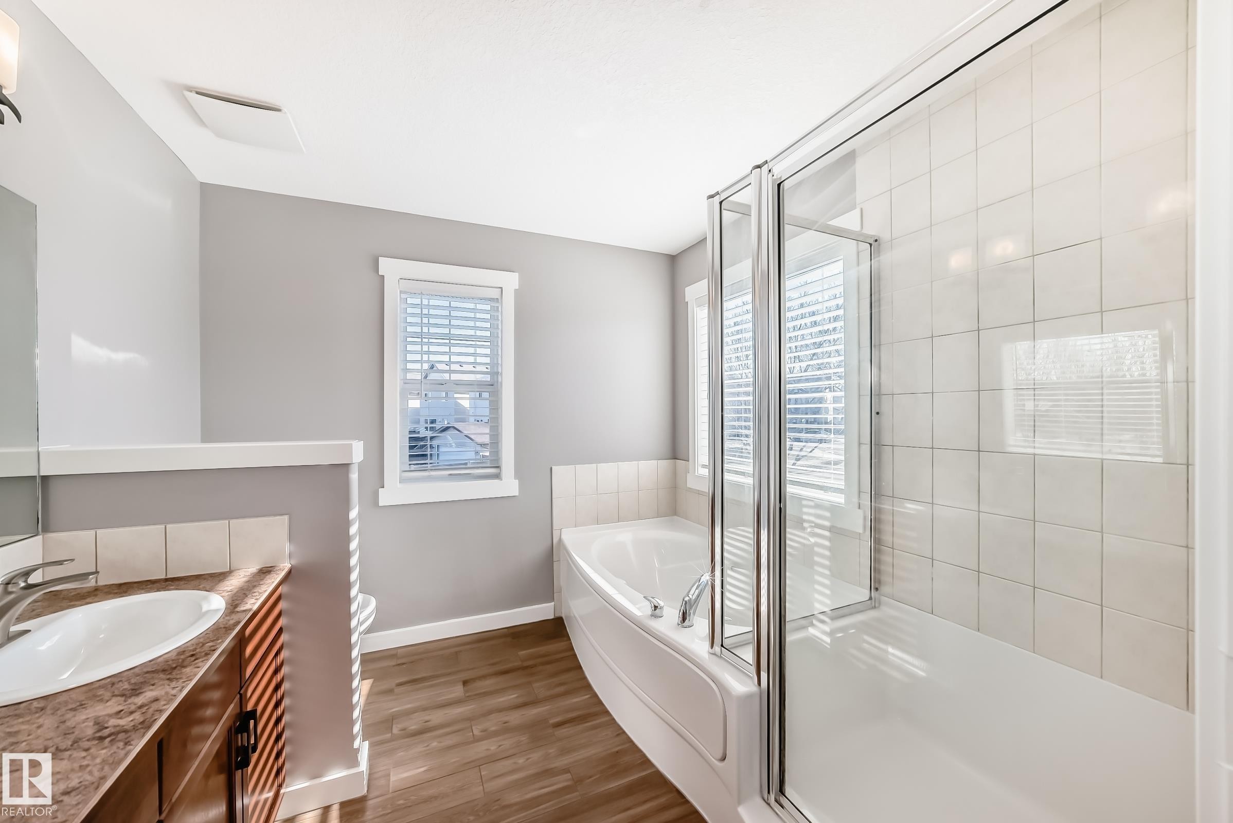 The bathroom features a vanity with a white oval sink, a built-in bathtub with a shower enclosure, and a window with blinds - 6303 2 Avenue, Edmonton, AB - Indoor Photo Showing Bathroom