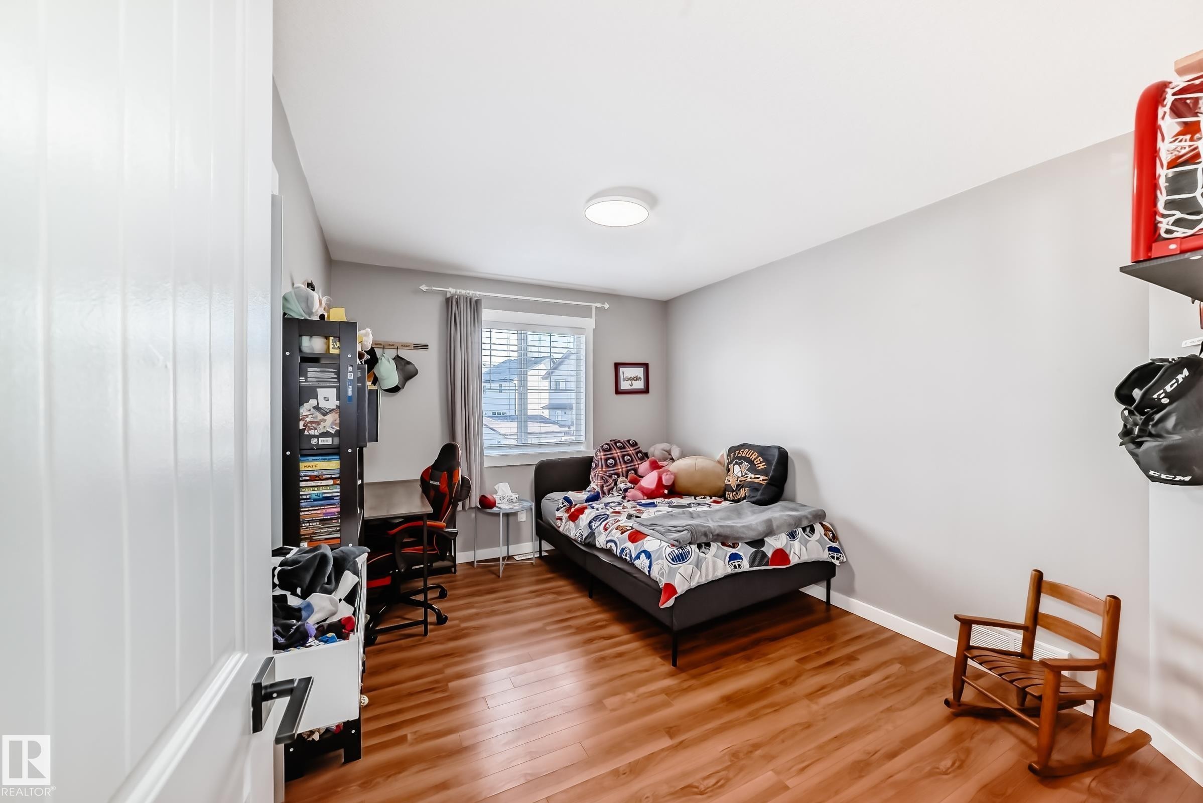 This room features wood flooring, light grey walls, and a window with white blinds and grey curtains - 6303 2 Avenue, Edmonton, AB - Indoor Photo Showing Bedroom