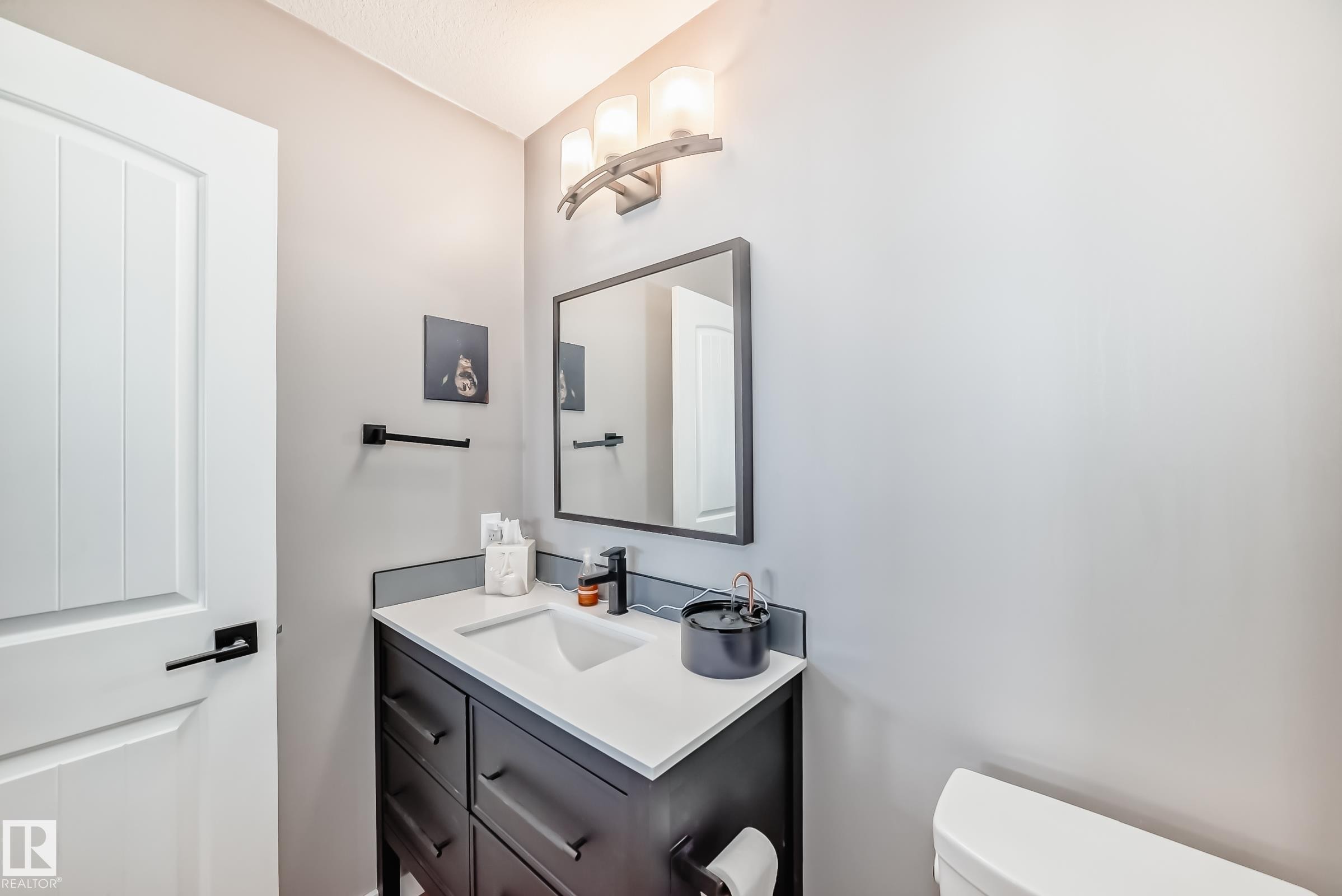 The bathroom features a vanity with a white countertop and a dark cabinet, complete with a contemporary faucet and a framed mirror - 6303 2 Avenue, Edmonton, AB - Indoor Photo Showing Bathroom