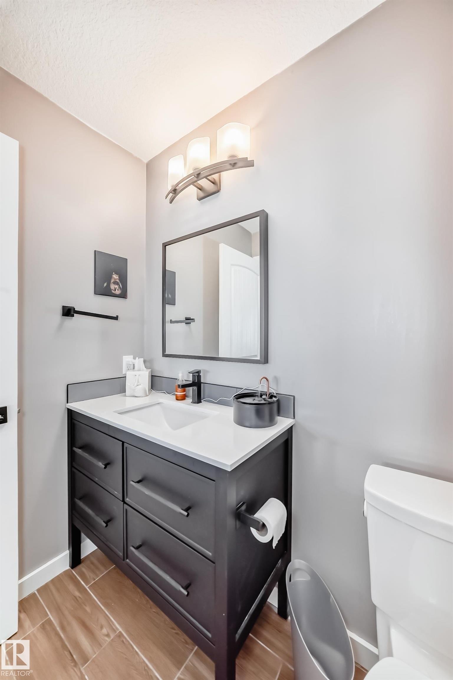 Bathroom featuring a dark wood vanity with a white countertop and a rectangular sink, complemented by a wall-mounted mirror - 6303 2 Avenue, Edmonton, AB - Indoor Photo Showing Bathroom