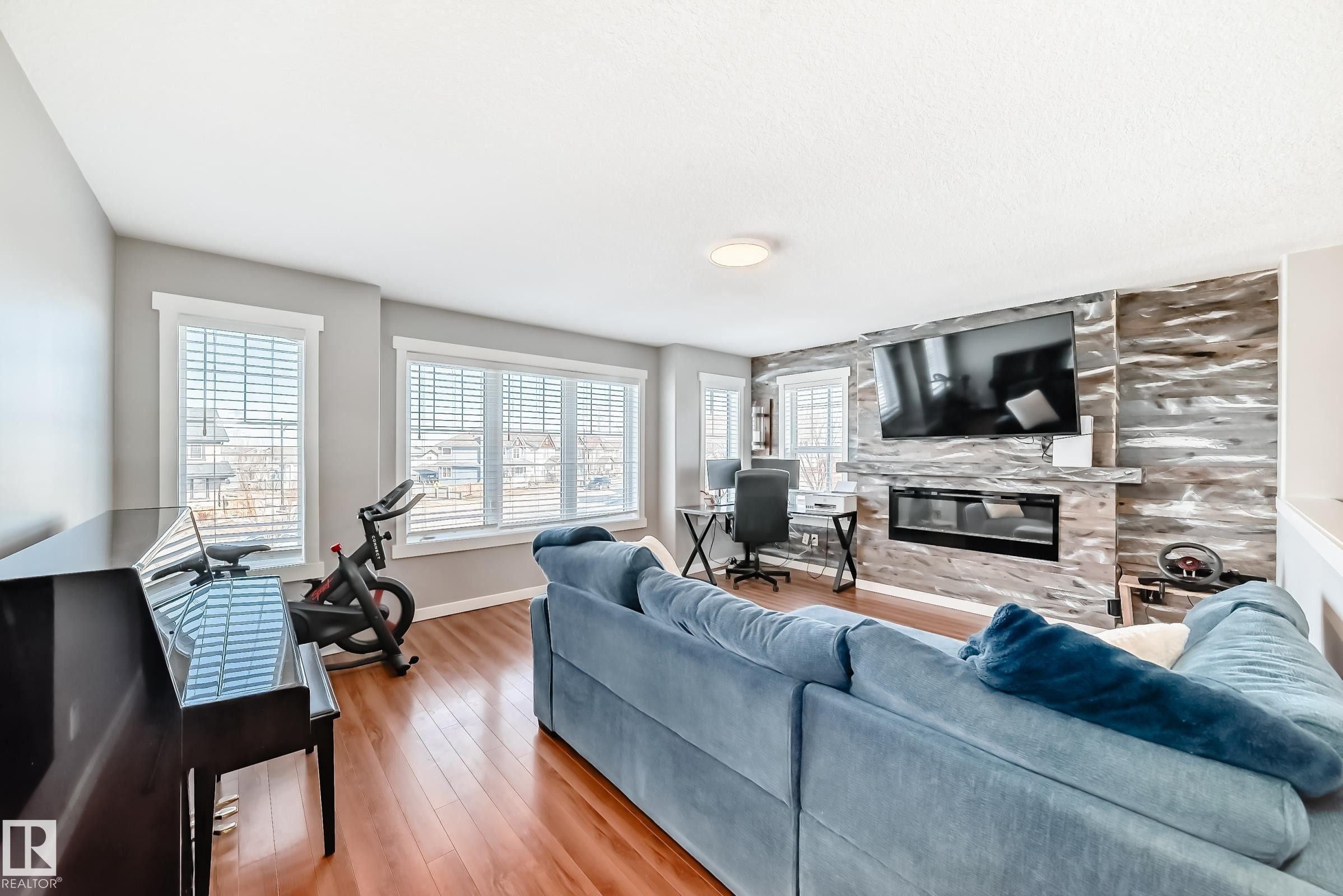 The living area features hardwood floors, a stone accent wall, and an electric fireplace - 6303 2 Avenue, Edmonton, AB - Indoor Photo Showing Living Room With Fireplace
