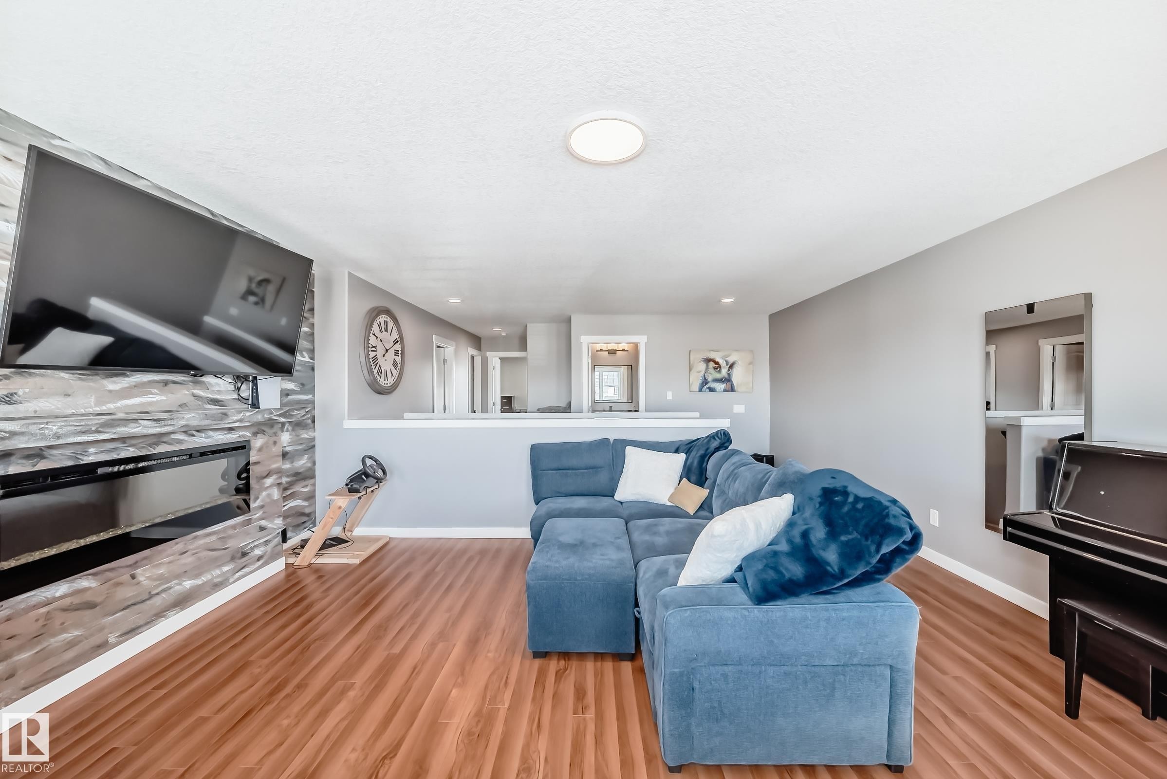 Living area featuring wood-look flooring, a fireplace with a stone surround, and light gray walls - 6303 2 Avenue, Edmonton, AB - Indoor Photo Showing Living Room With Fireplace