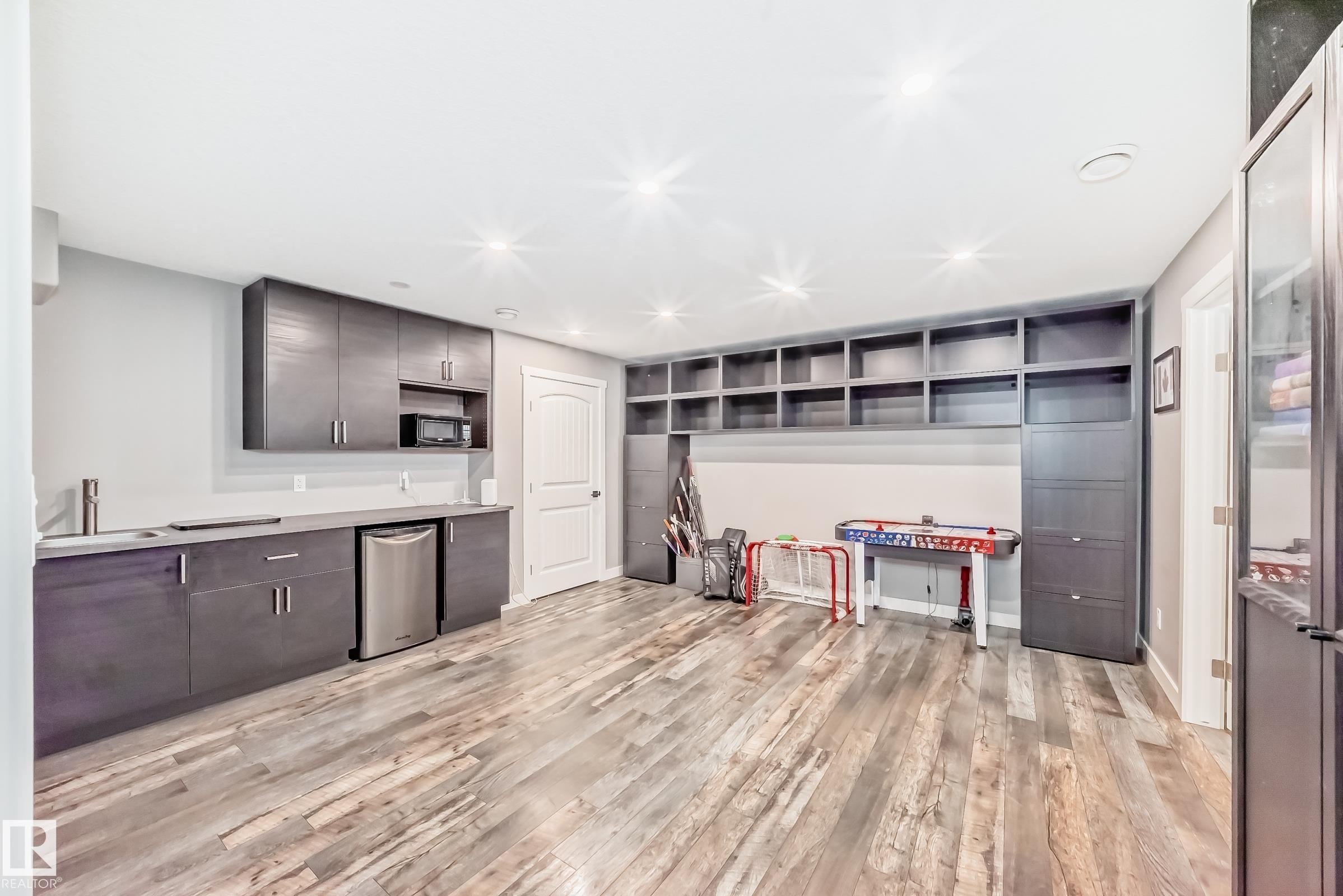 This versatile room features extensive built-in shelving, durable wood-look flooring, and recessed ceiling lighting - 6303 2 Avenue, Edmonton, AB - Indoor