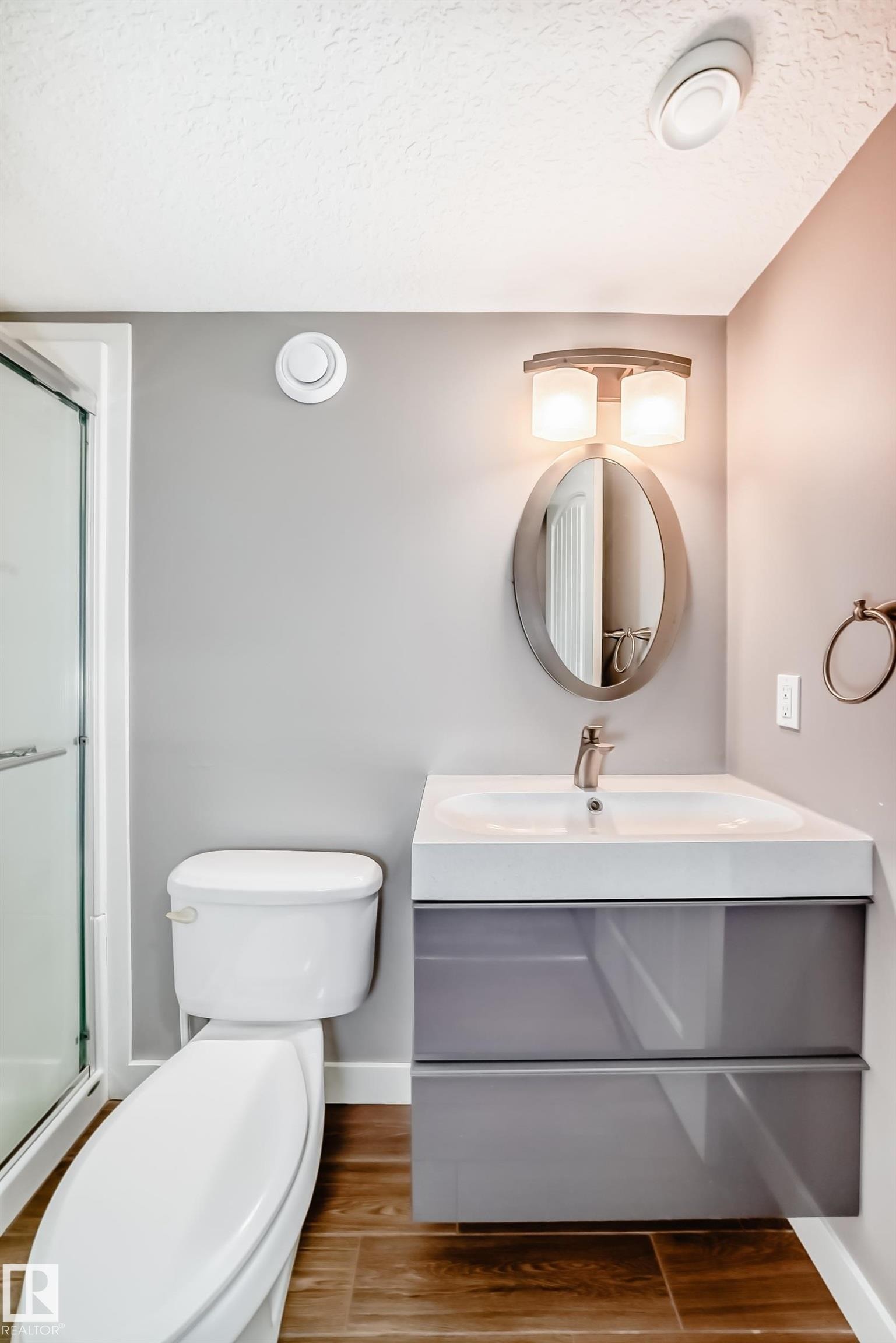 Bathroom featuring a white toilet, a modern floating vanity with a white countertop and basin, and a mirrored medicine cabinet with an overhead light fixture - 6303 2 Avenue, Edmonton, AB - Indoor Photo Showing Bathroom