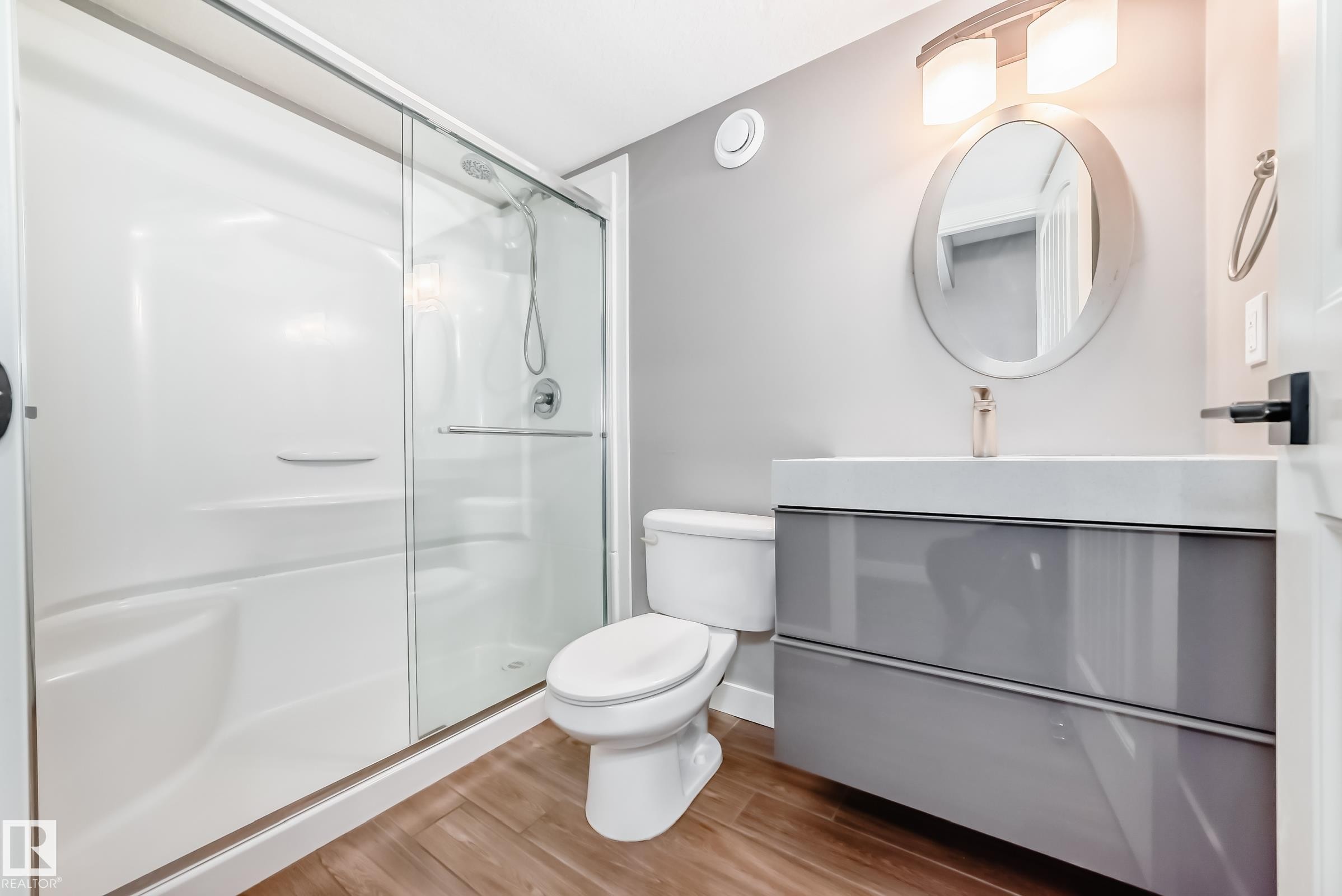 The bathroom features a modern vanity with a rectangular basin, a circular mirror, and a shower with a sliding glass door - 6303 2 Avenue, Edmonton, AB - Indoor Photo Showing Bathroom