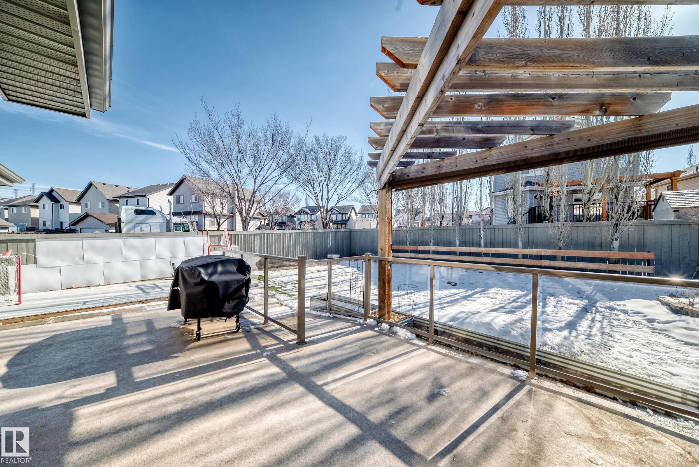 The property features a concrete patio area with a wooden pergola, equipped with a clear glass railing system - 6303 2 Avenue, Edmonton, AB - Outdoor