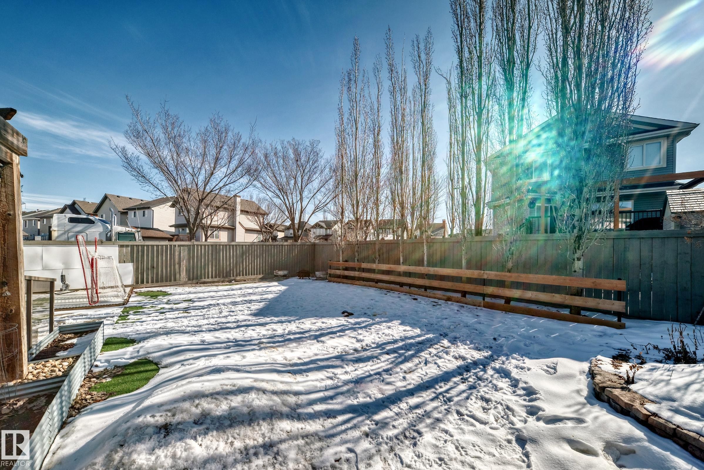 The property features a fenced backyard with a snow-covered lawn, a stone-lined garden bed, and a raised garden bed with corrugated metal and artificial turf accents - 6303 2 Avenue, Edmonton, AB - Outdoor